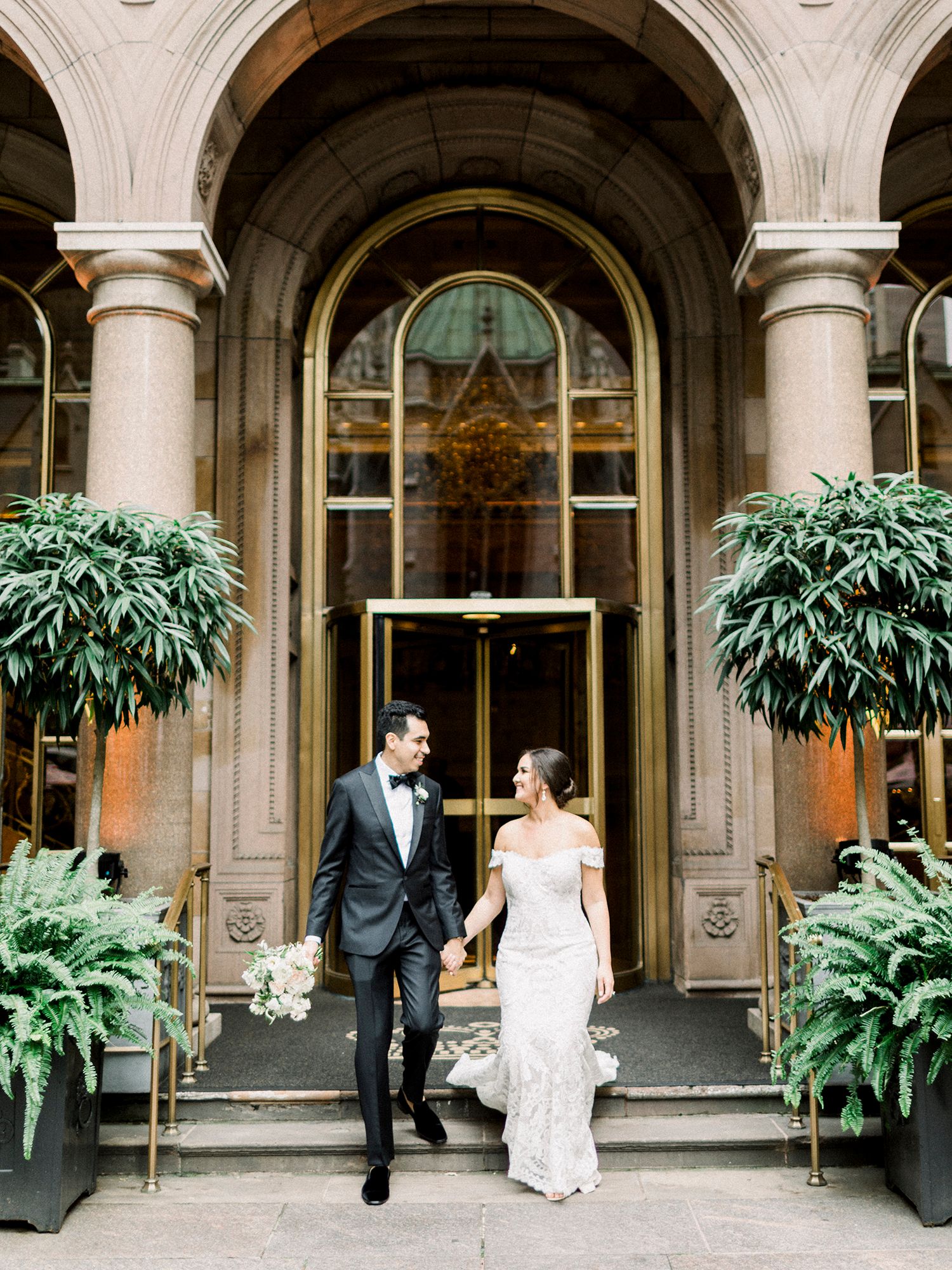 Elegant stone archways and columns frame a covered walkway with potted plants and classic architectural details.