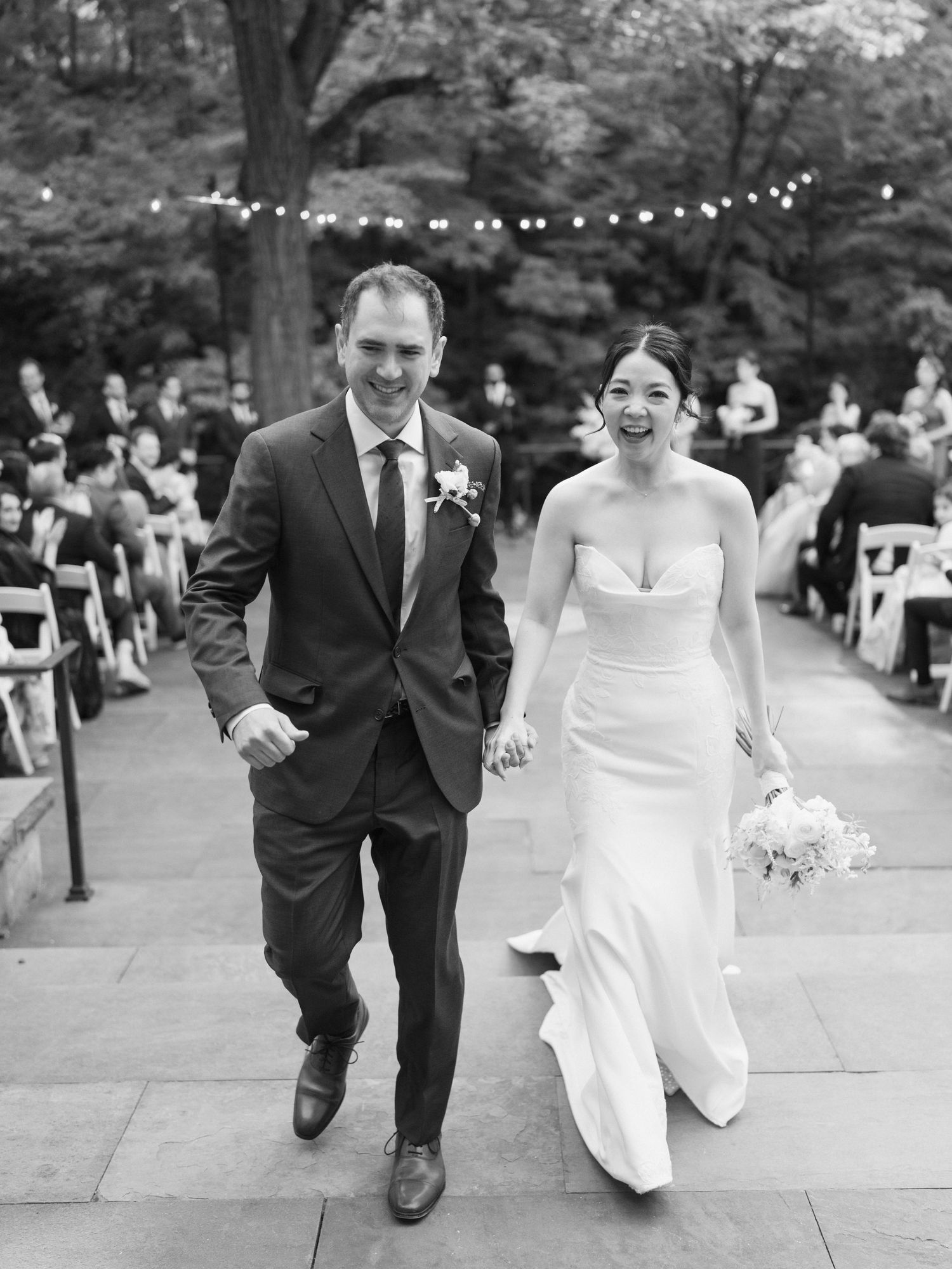 A joyful exit down a stone pathway lined with guests and string lights overhead.