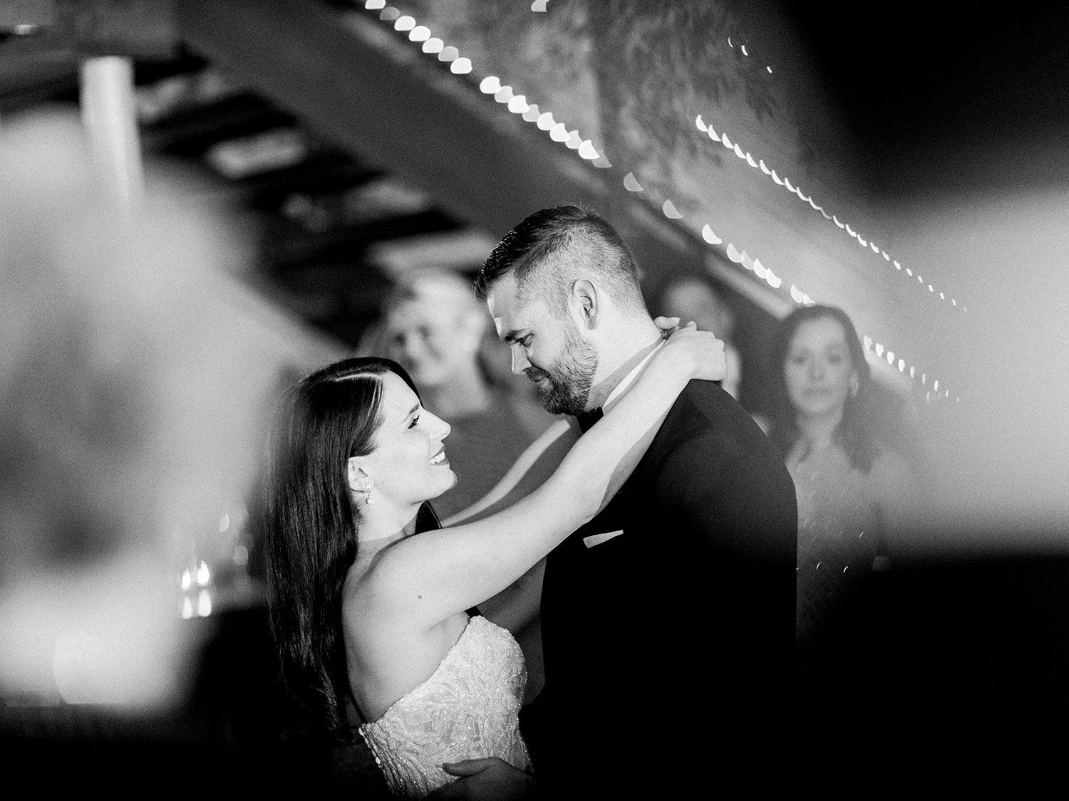 Romantic couples dancing under twinkling lights at an evening celebration.