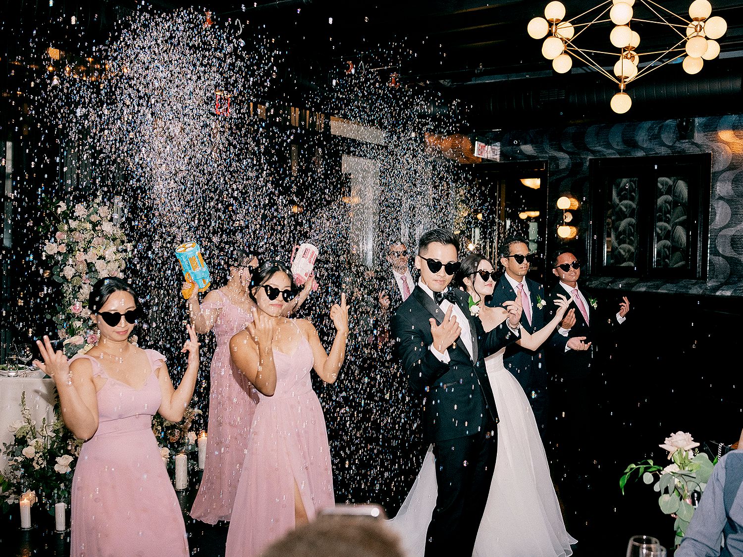 Wedding party celebrates with sparklers in a dark venue creating a festive atmosphere. NYC wedding photographer.