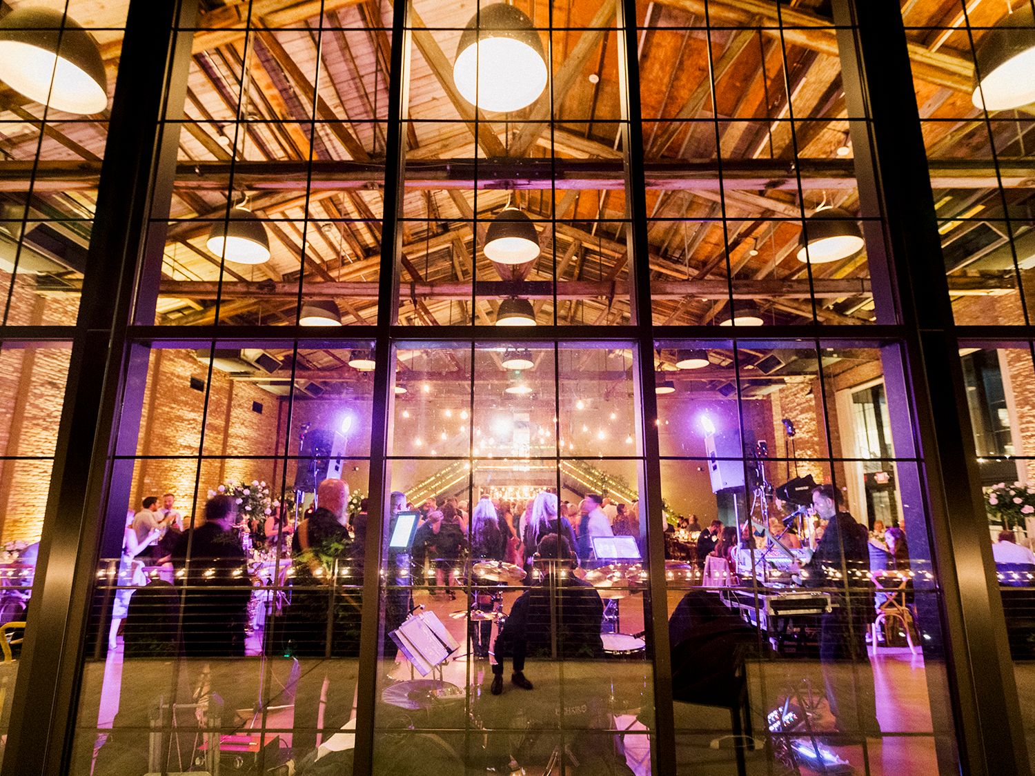 Industrial venue space illuminated with purple uplighting and string lights for an evening celebration. NYC wedding photographer.