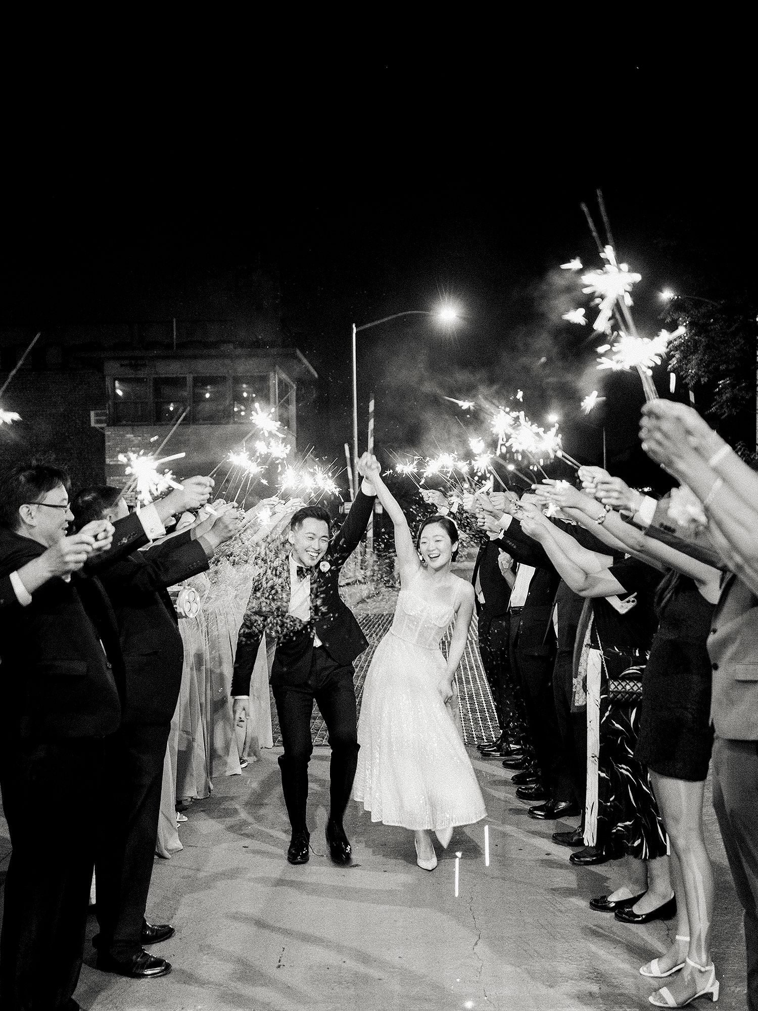 Wedding couple exits through a sparkler tunnel lined with guests in black and white photography. NYC wedding photographer.