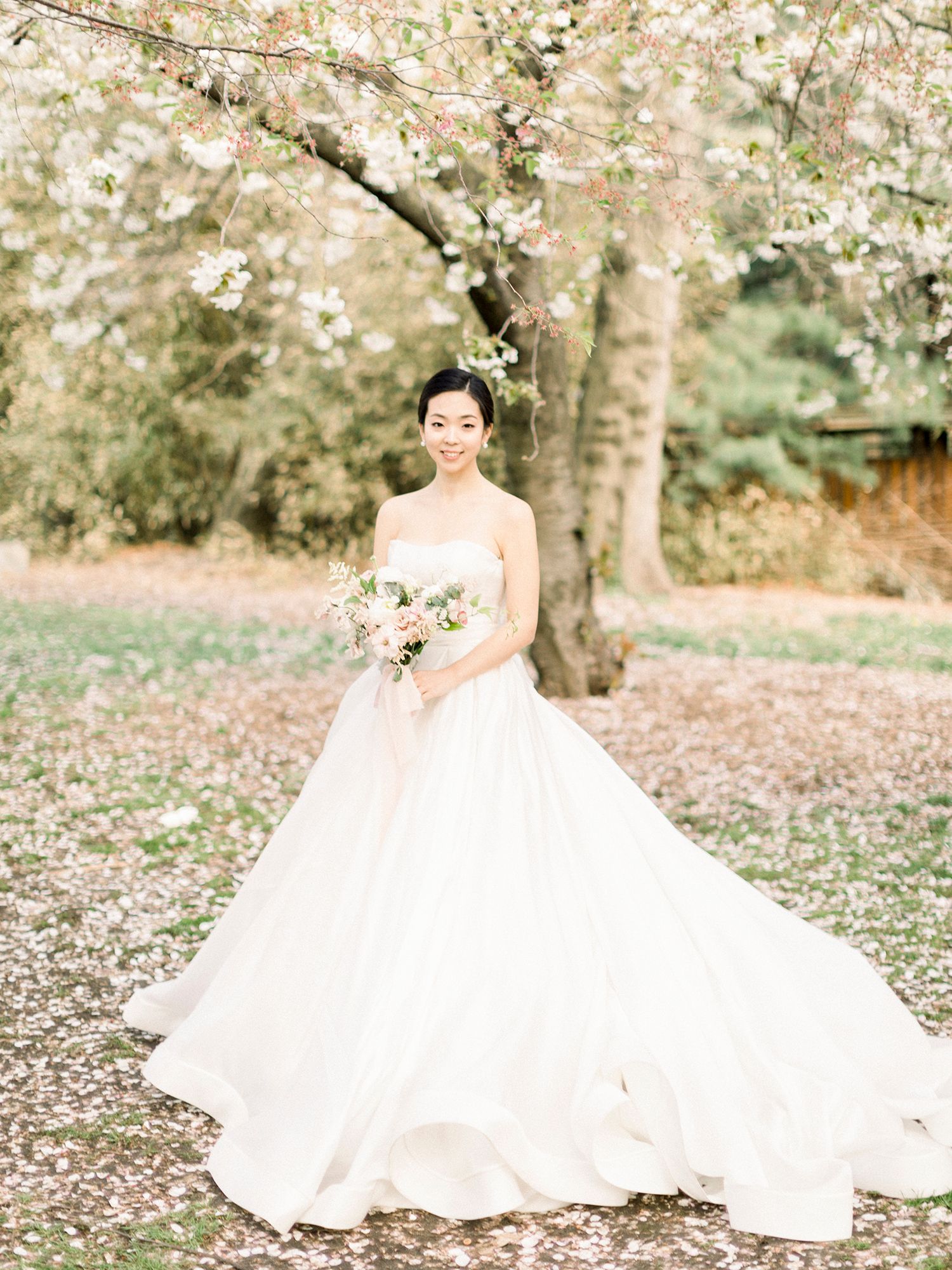 Elegant bridal portraits under blooming cherry trees with a voluminous white wedding dress.