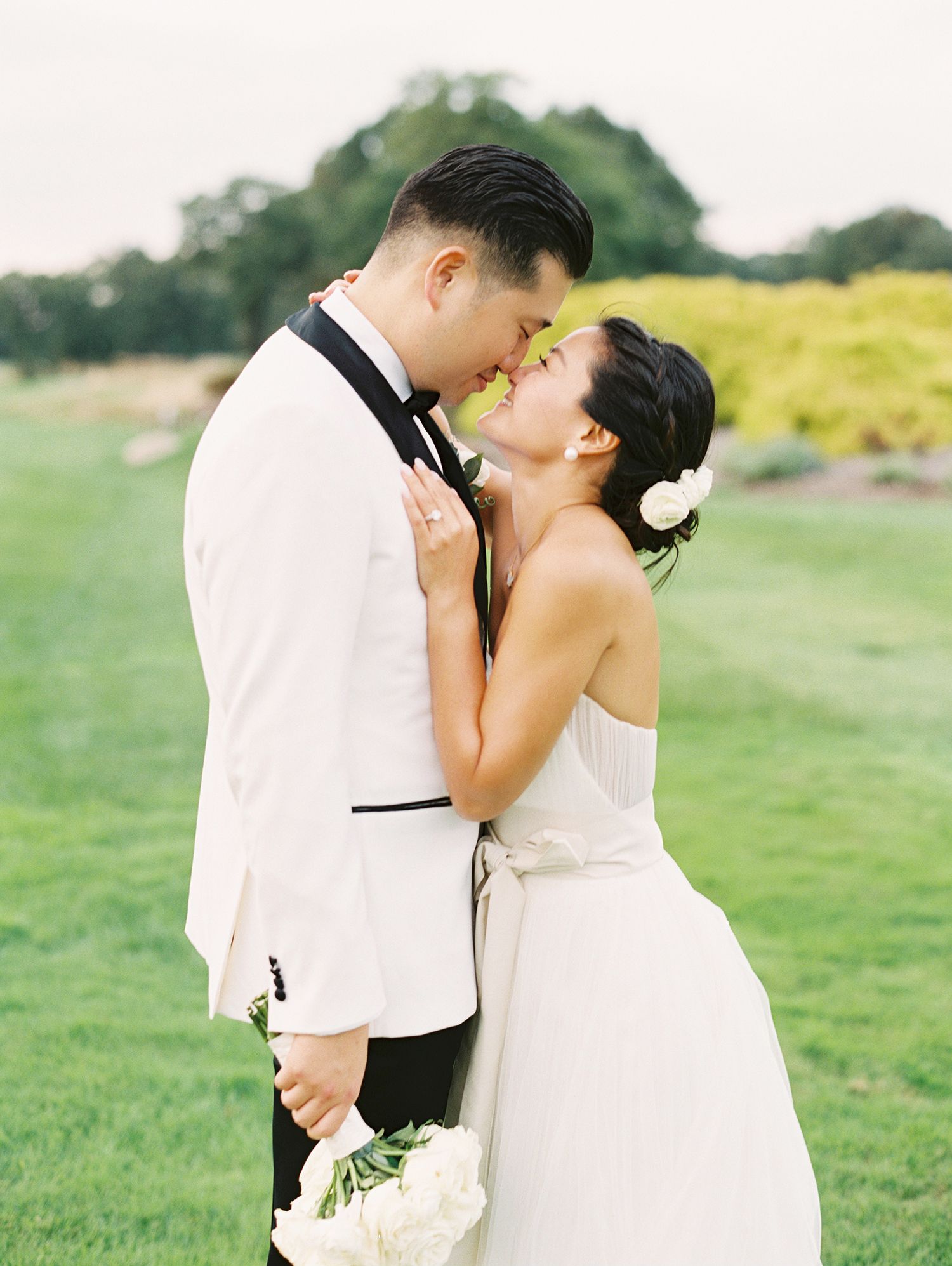 Romantic wedding couple embraces in a sunlit green field.