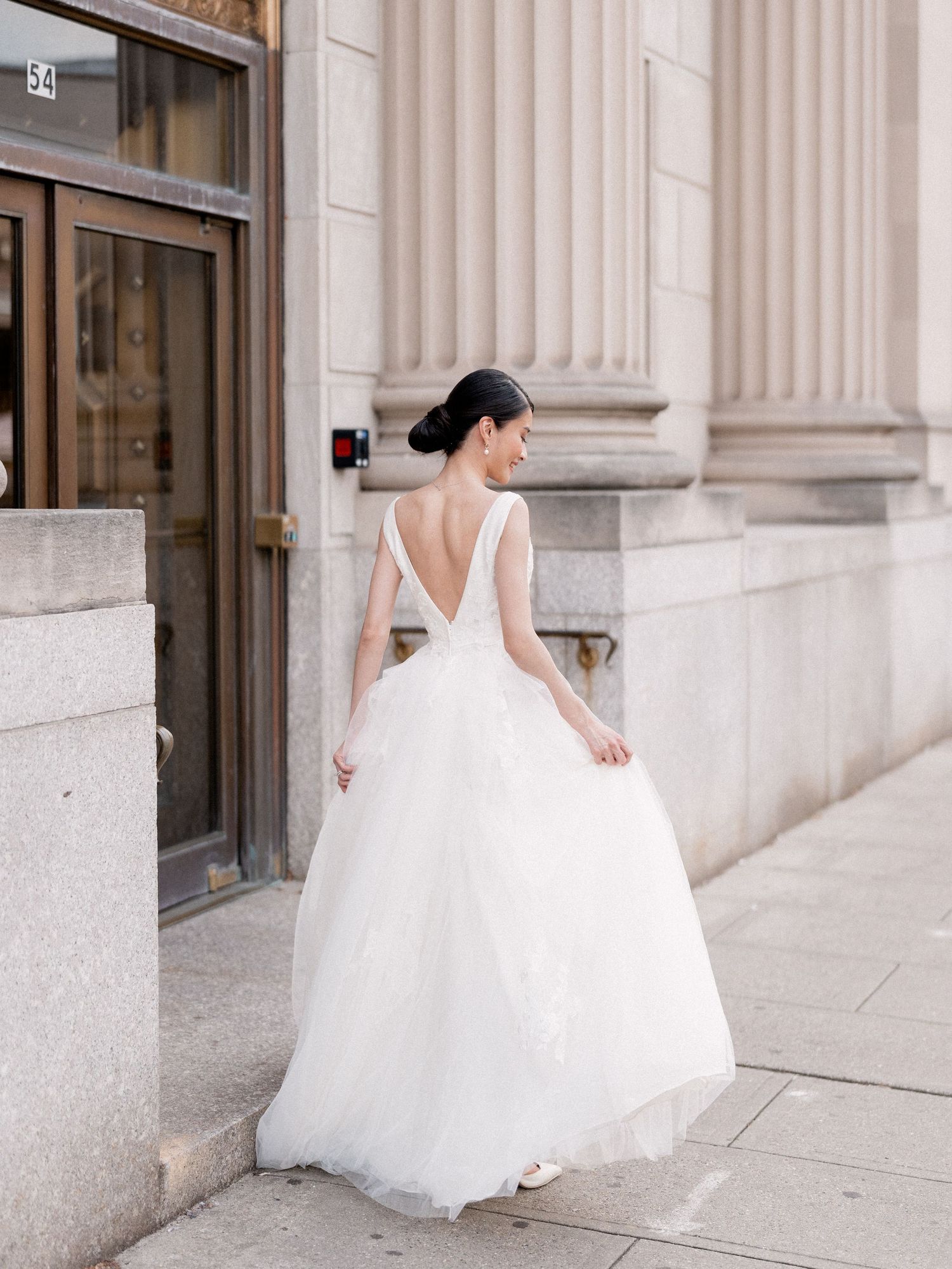 A bride in a flowing white ballgown twirls between elegant stone columns.