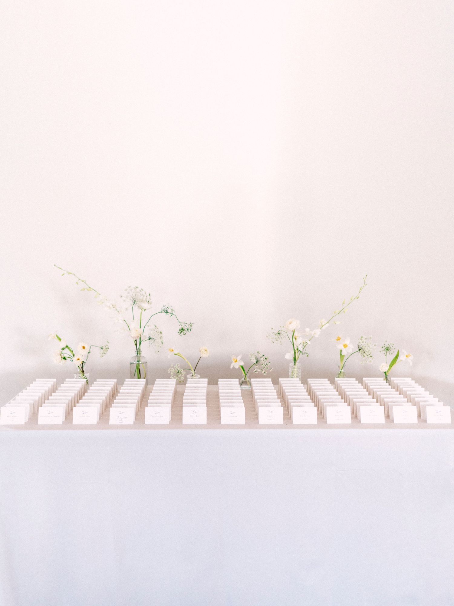 Minimalist white table settings with delicate floral arrangements and place cards.