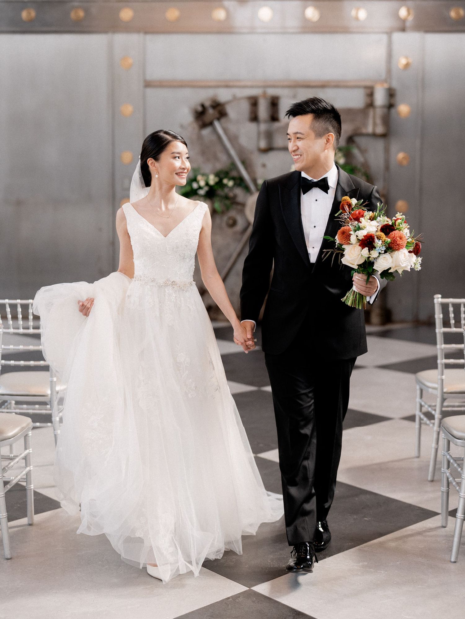 Couple dancing together in an elegant venue with string lights and white chairs in the background.
