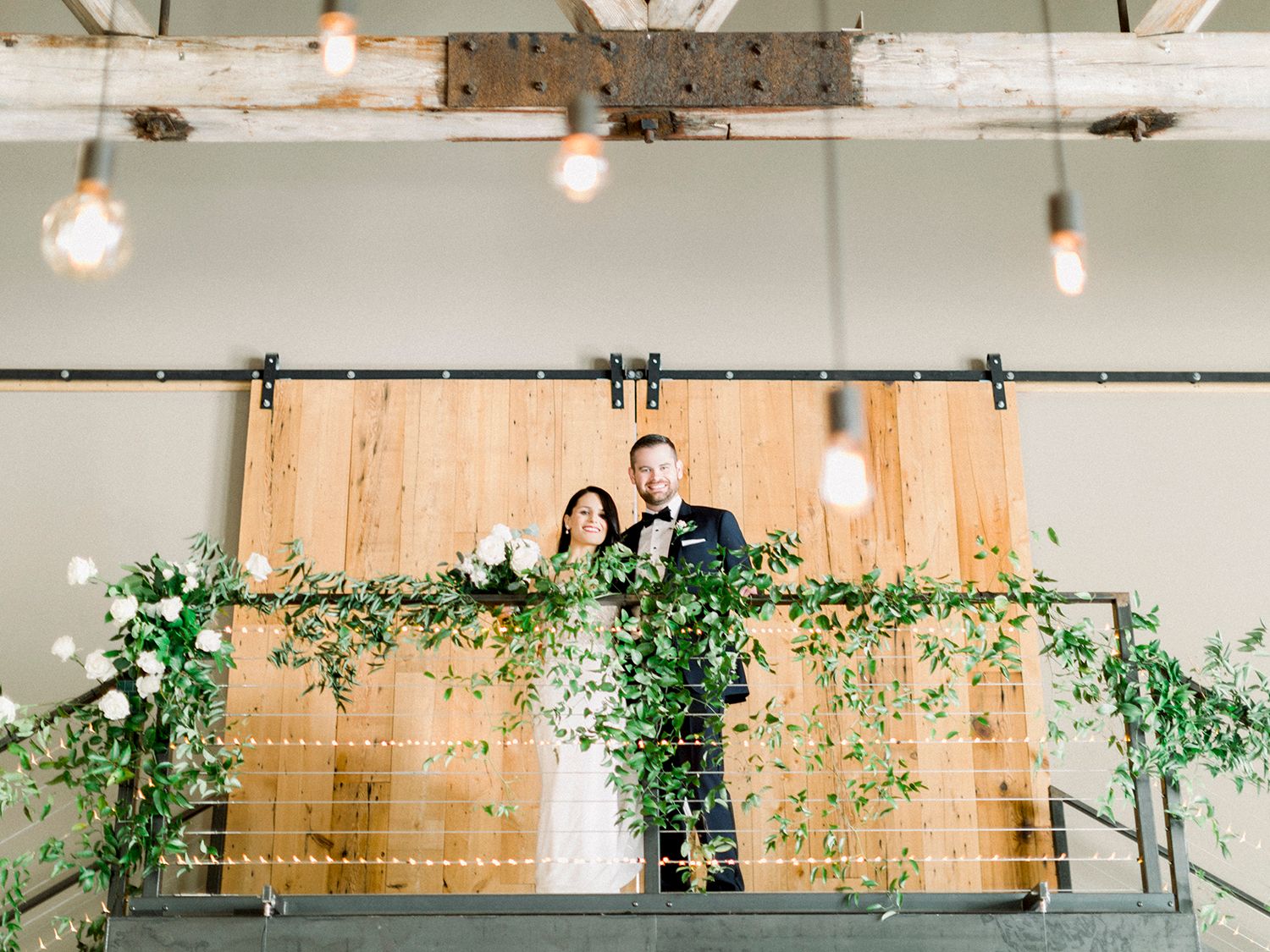 Modern industrial wedding venue decorated with string lights and climbing greenery.
