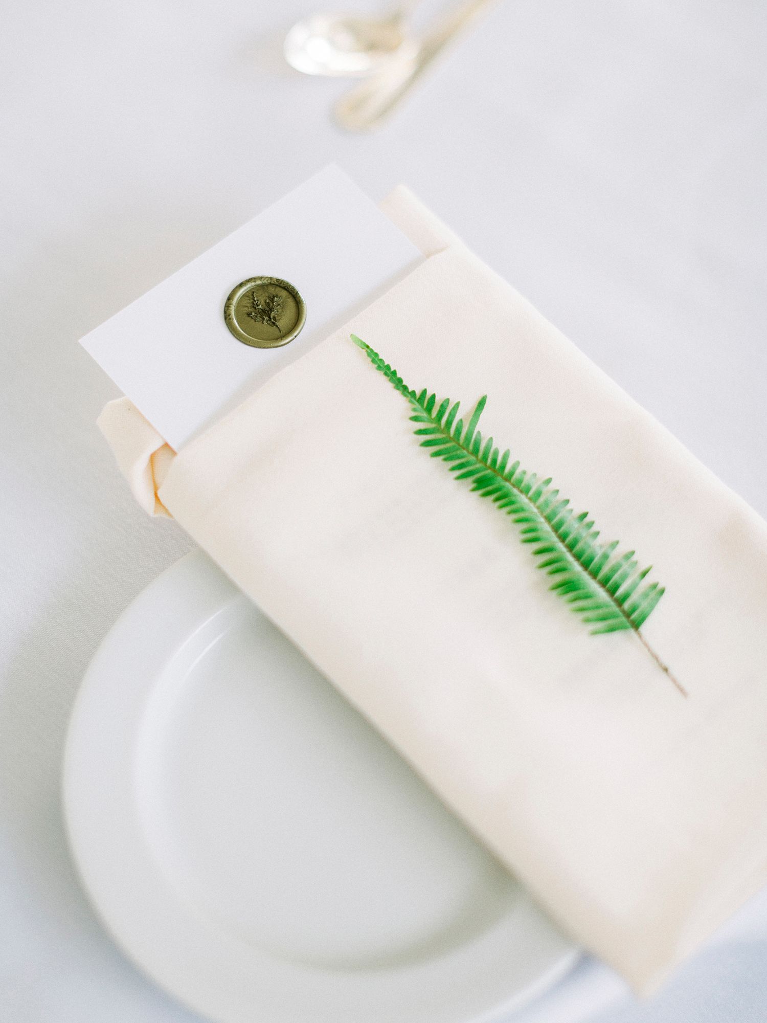 Simple white place settings with delicate green fern leaf accents on crisp linens.