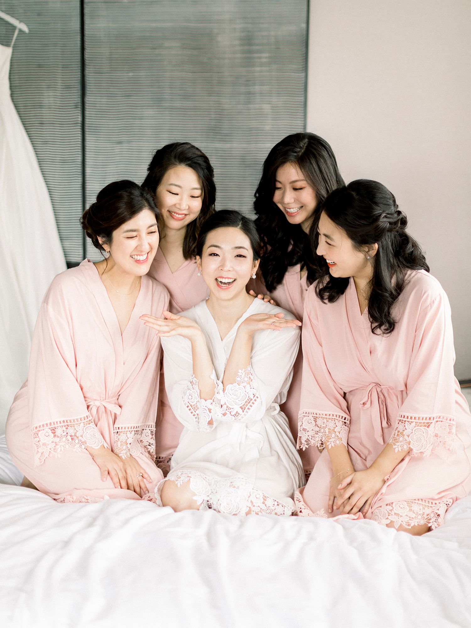 Group wearing pink robes share joyful moments together on a white bed.