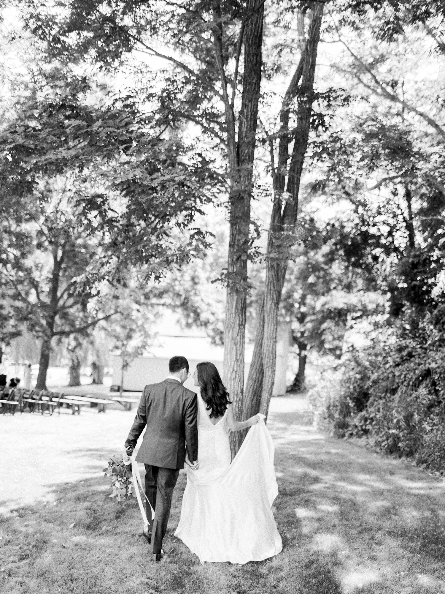 A couple walks through a tree-lined path in black and white wedding photography.