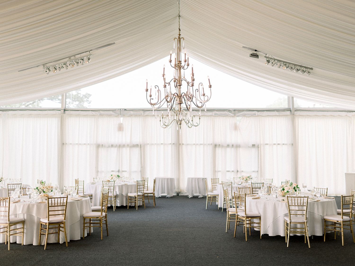 Elegant white wedding reception venue with crystal chandeliers and draped fabric decorating a spacious ballroom.