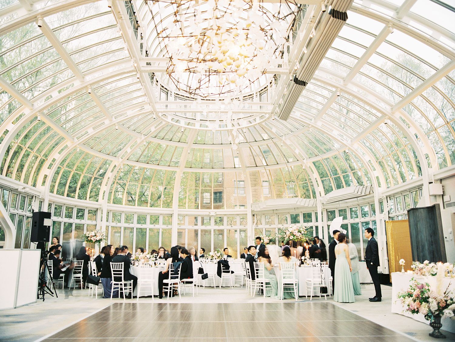 Sunlit conservatory venue with white chairs arranged for an elegant wedding ceremony. NYC wedding photographer.