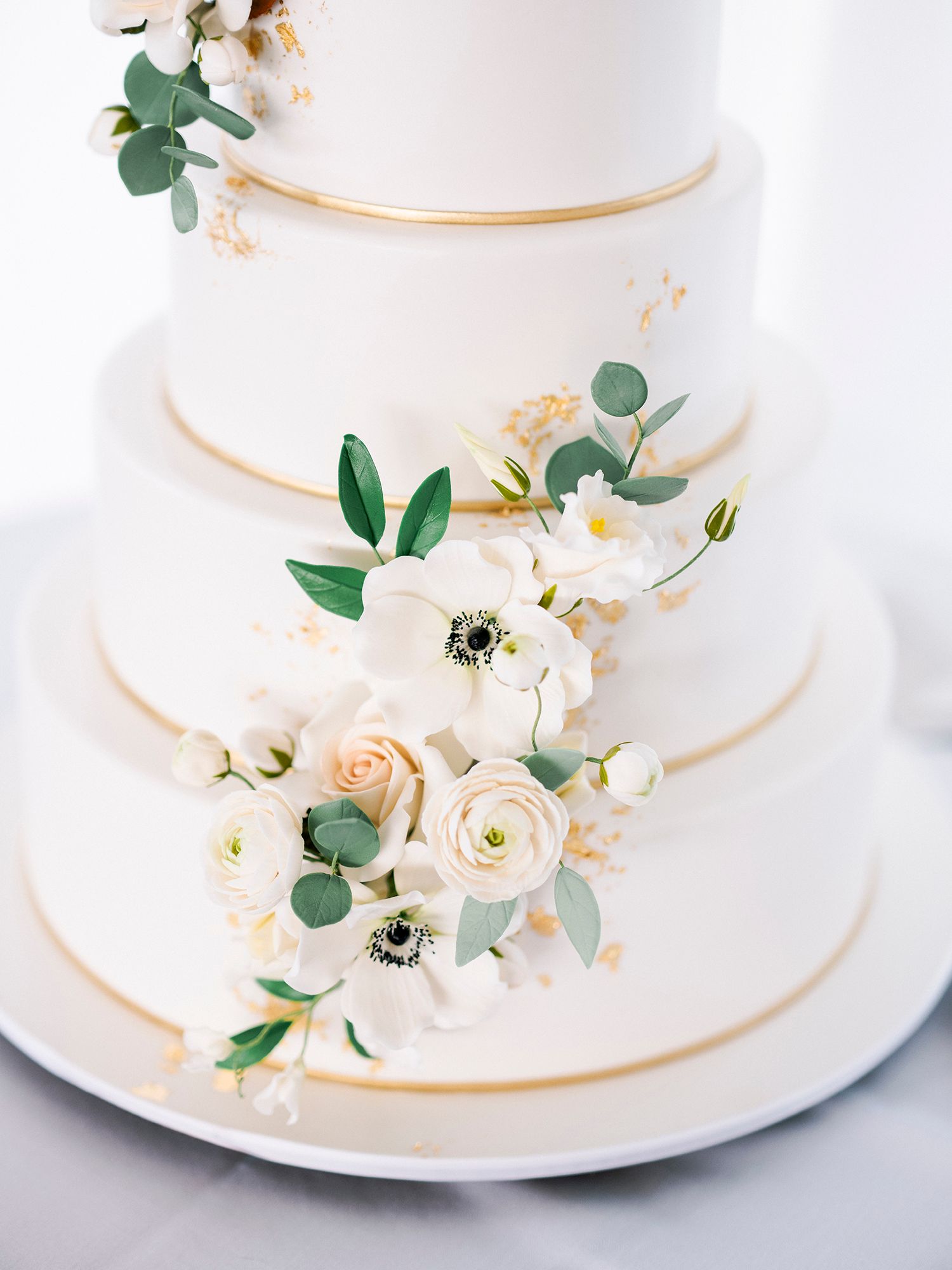 Elegant white tiered wedding cake decorated with fresh flowers and gold trim.