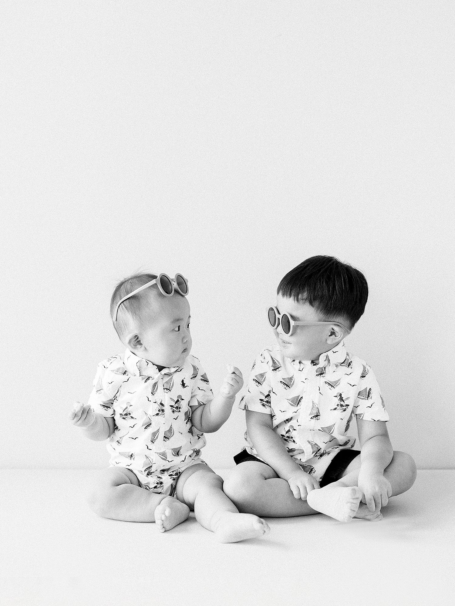 A series of four black and white photos showing babies in matching outfits sitting together on a white background.