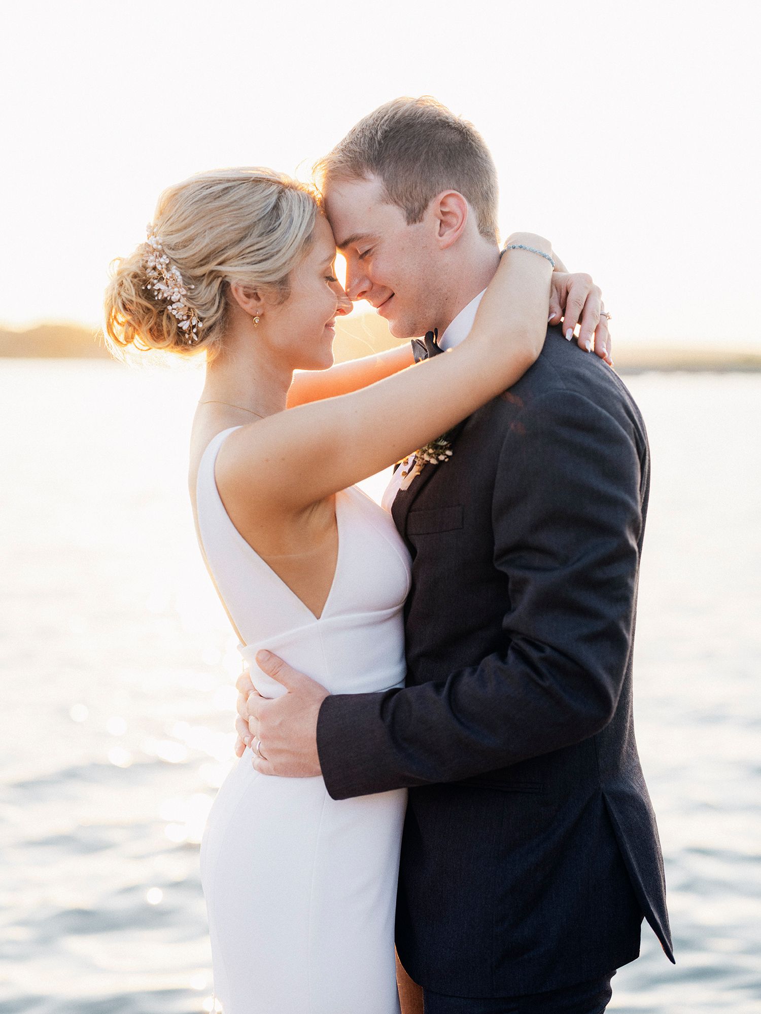 A couple shares an intimate moment at sunset by the water in their wedding attire. NYC wedding photographer.