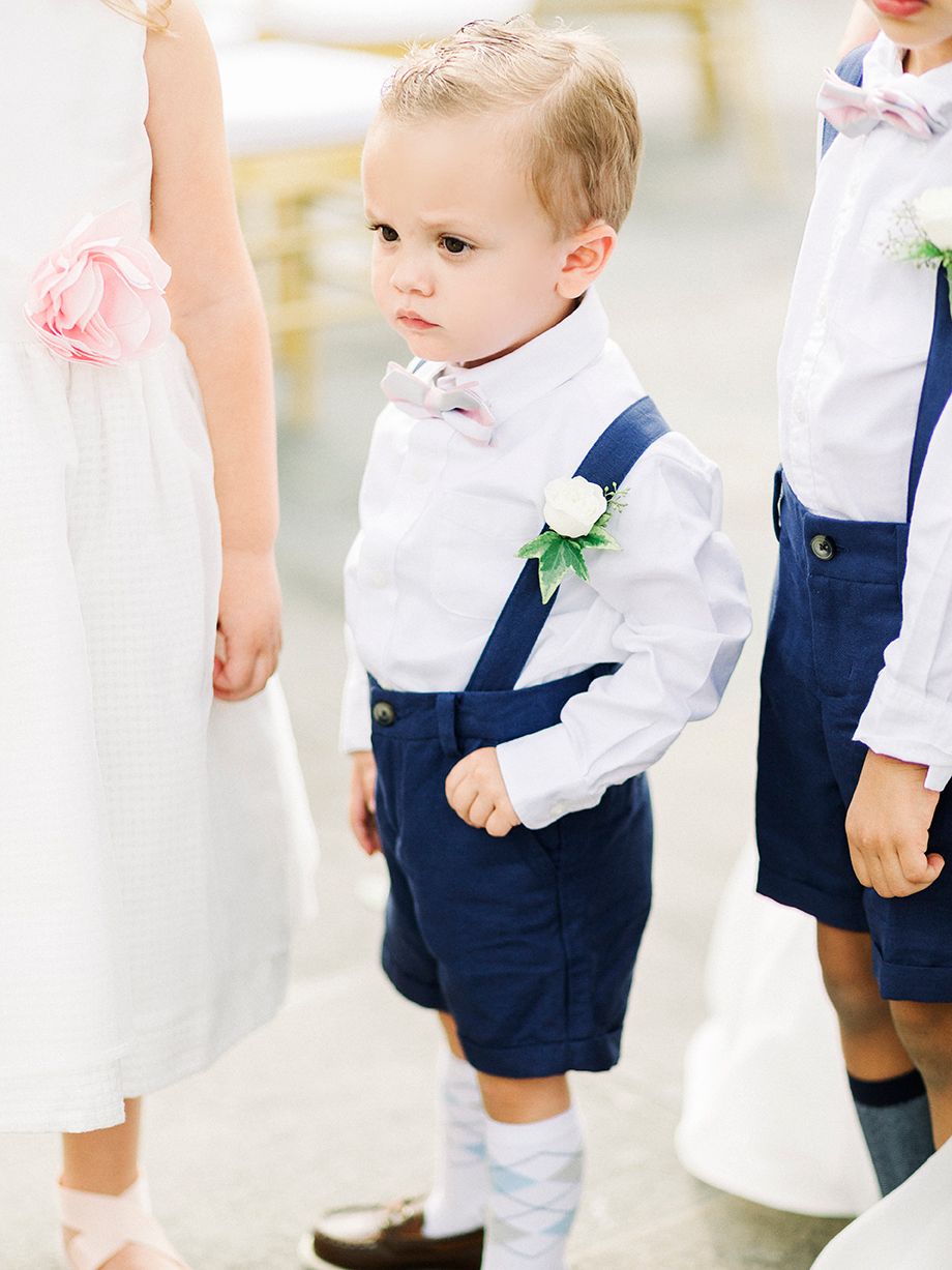 Young ring bearers in navy shorts and white shirts stand adorably at a wedding ceremony.