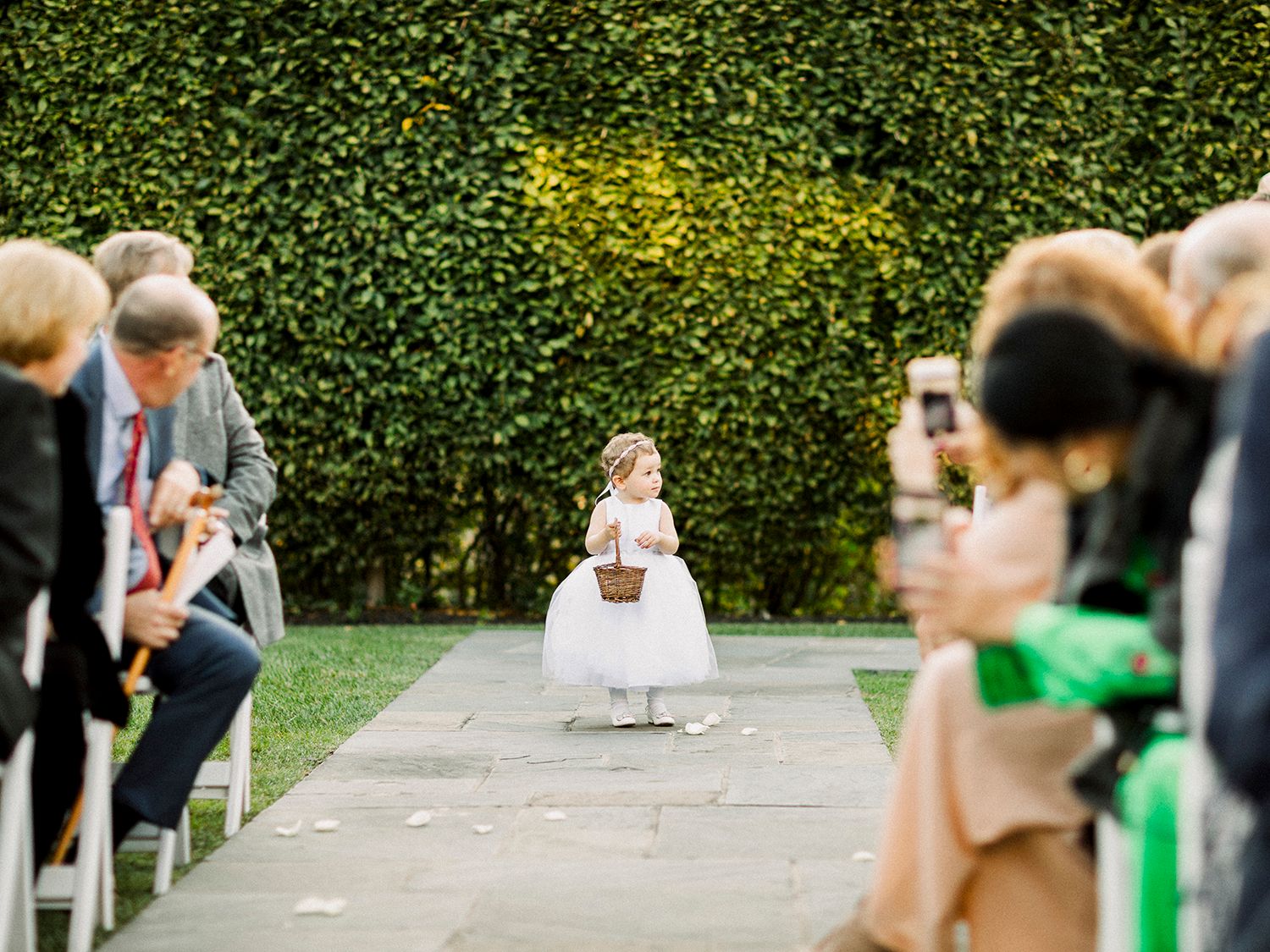 Outdoor wedding ceremony setup with white chairs and hedged garden backdrop.
