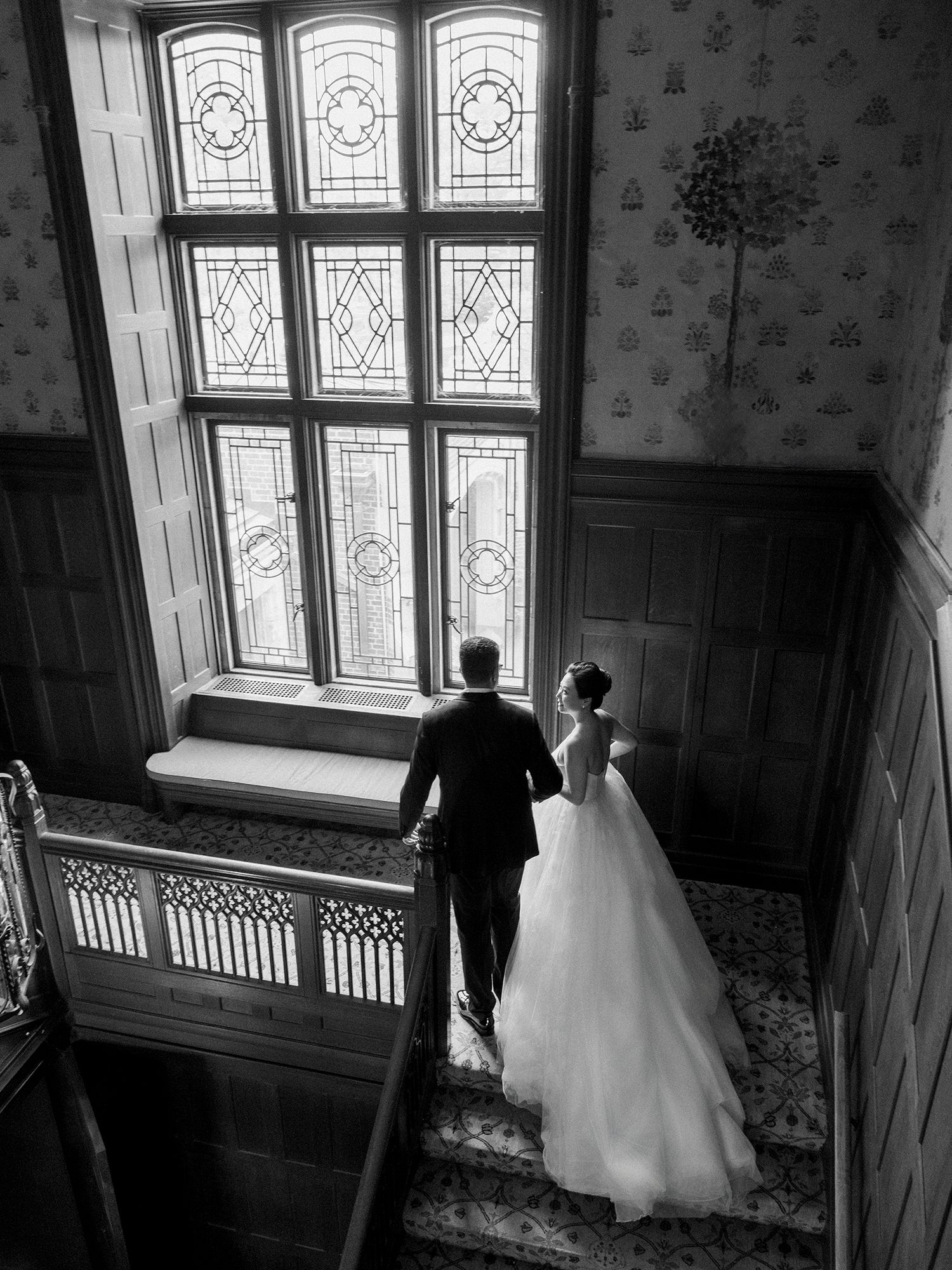 Couple in formal attire near ornate stained glass windows in vintage interior. NYC Wedding Photographer