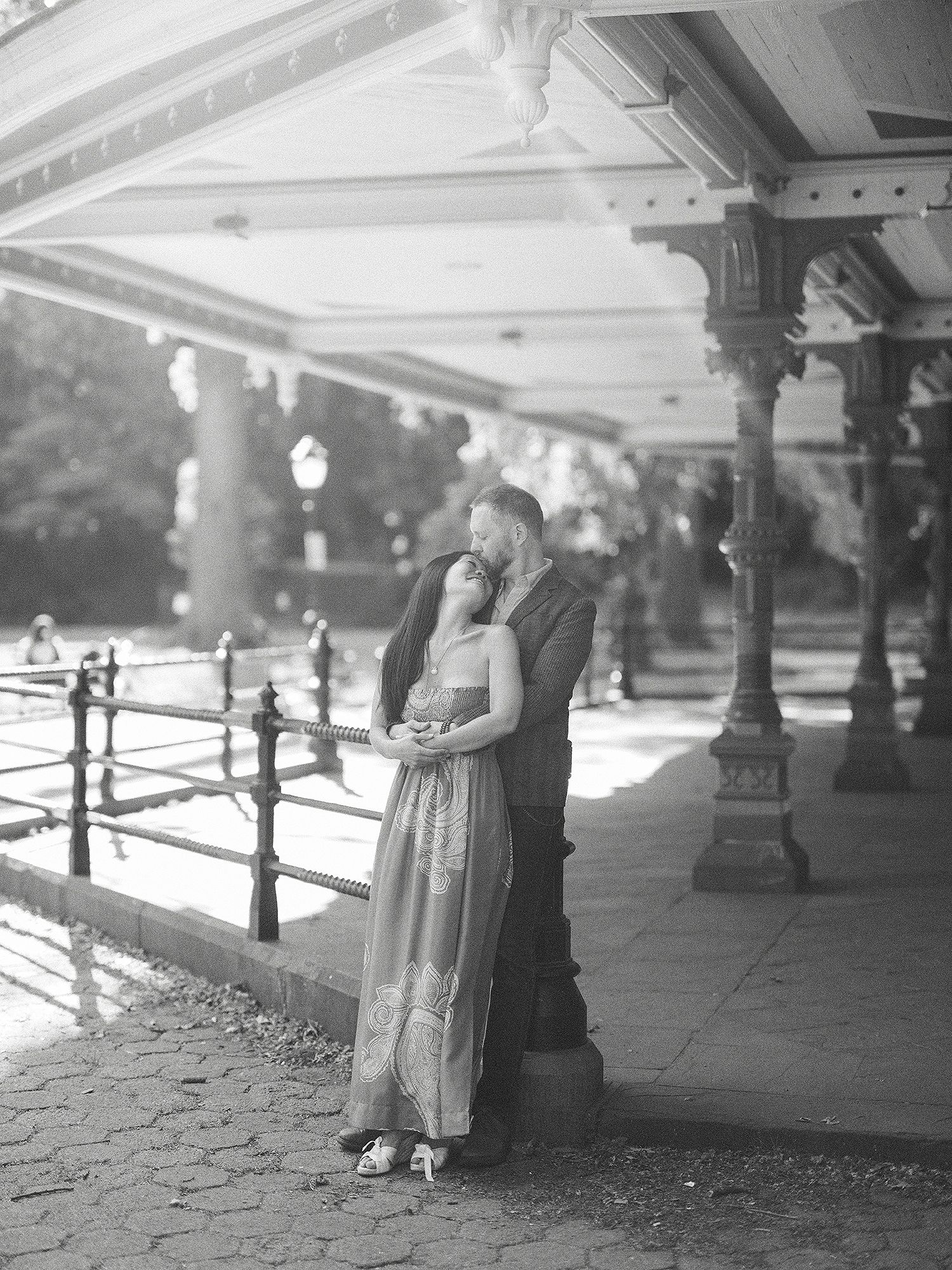 A couple shares an intimate moment under an ornate covered walkway in black and white.