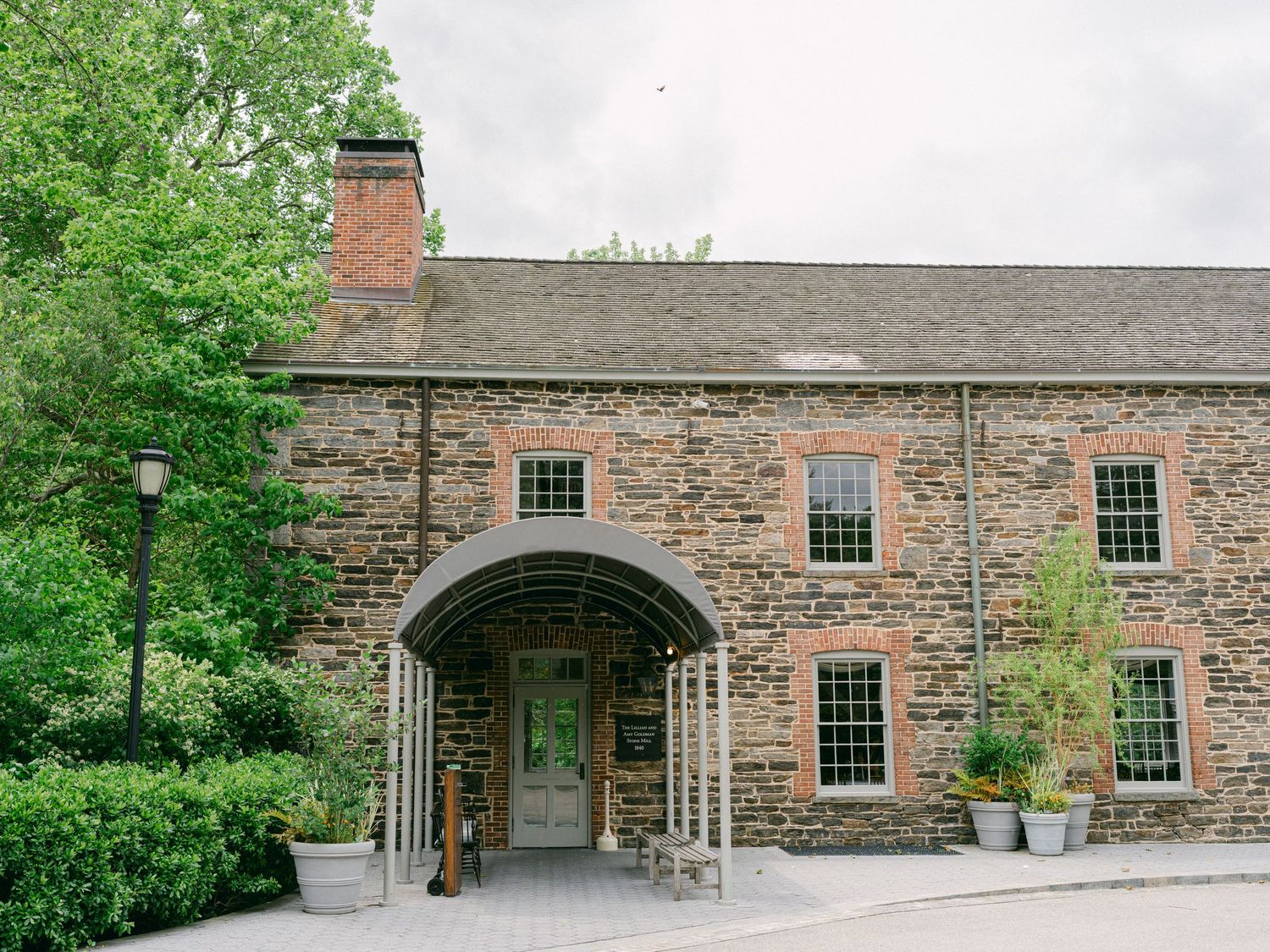 Historic stone building with multiple windows and archway entrance surrounded by greenery.