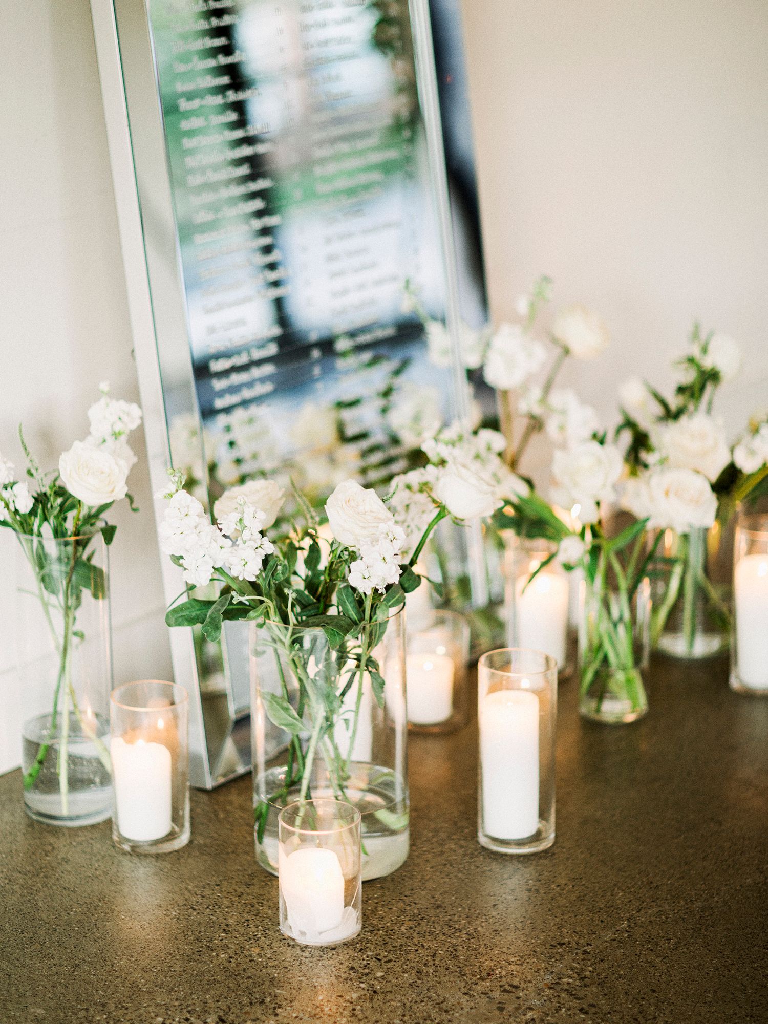 Simple elegant wedding decor featuring white flowers in glass vases with glowing candles.