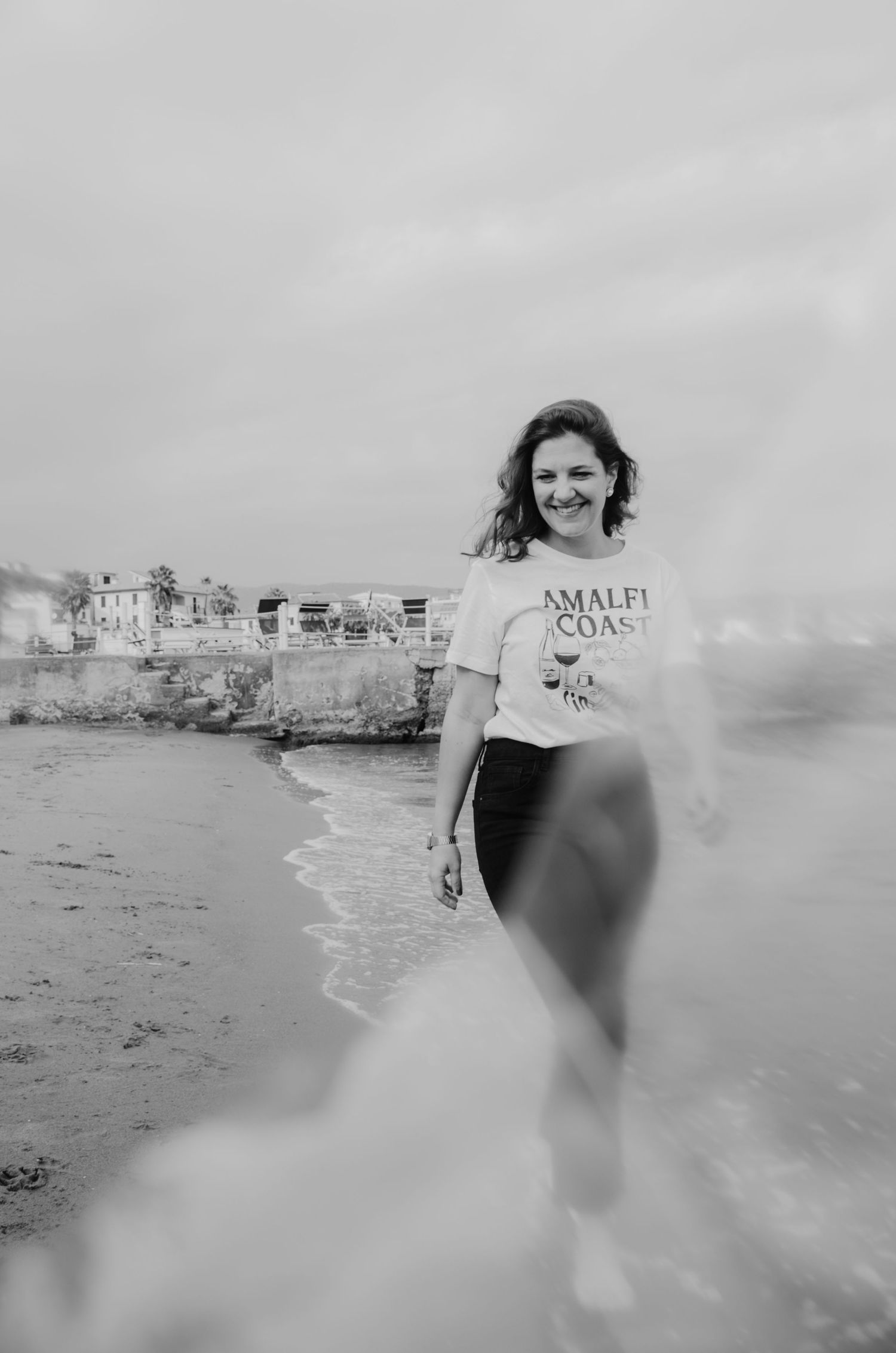 Schwarzweiß-Aufnahme einer Frau, die am Strand läuft. Dynamische Bewegung, Wind und Meer erzeugen eine freie, emotionale Bildstimmung.