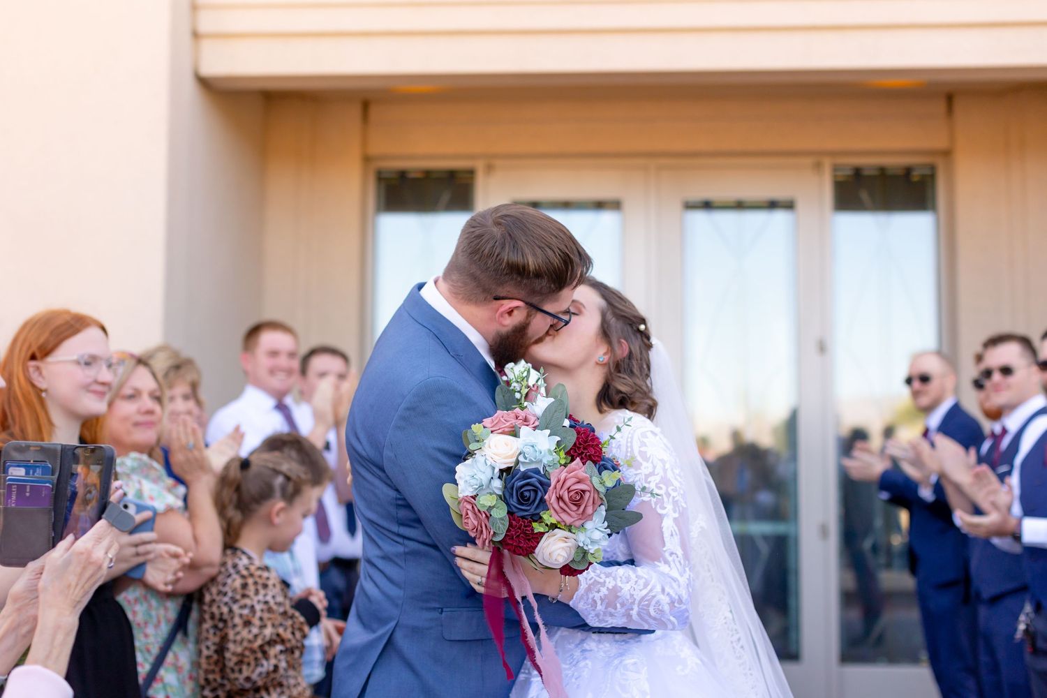 Arizona Wedding couple shares kiss on church steps as guests applaud in background.