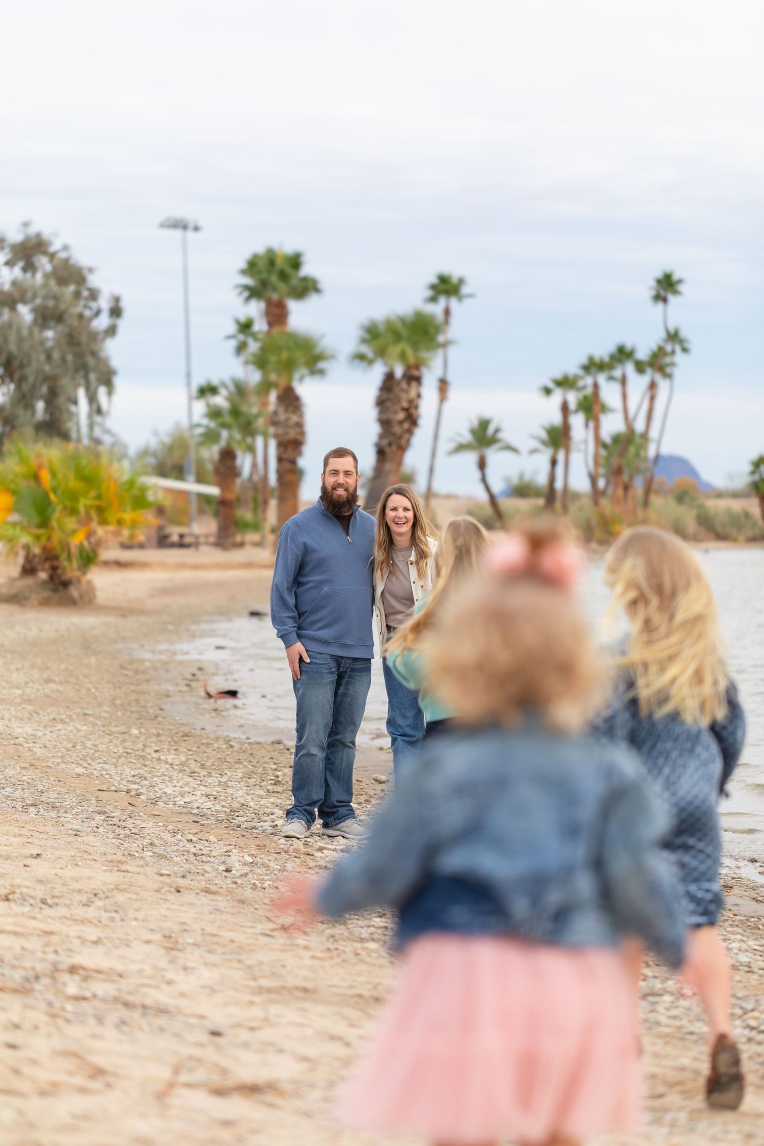 Parents watch their children play on rotary park beach in lake havasu city lined with palm trees.