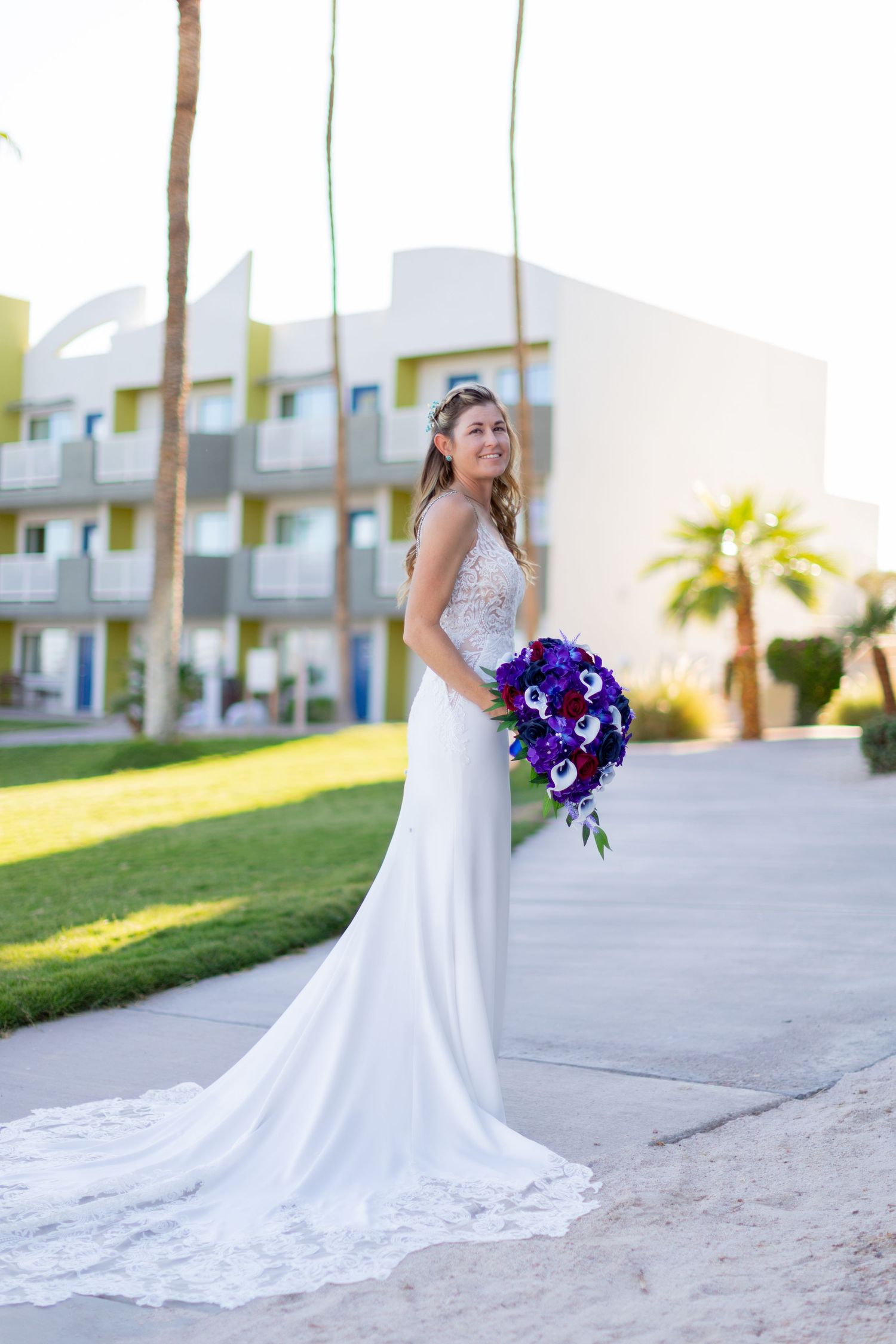 Bride in elegant white dress holds vibrant purple and blue bouquet against palm tree landscape at the nautical beachfront resort lake havasu