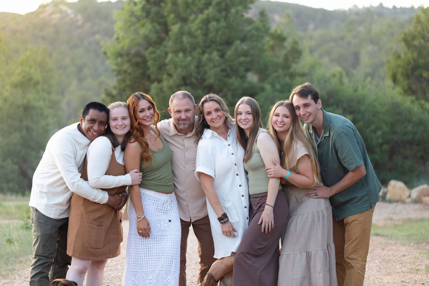 A group of people in coordinated casual outfits laugh together while posing outdoors in a natural setting.