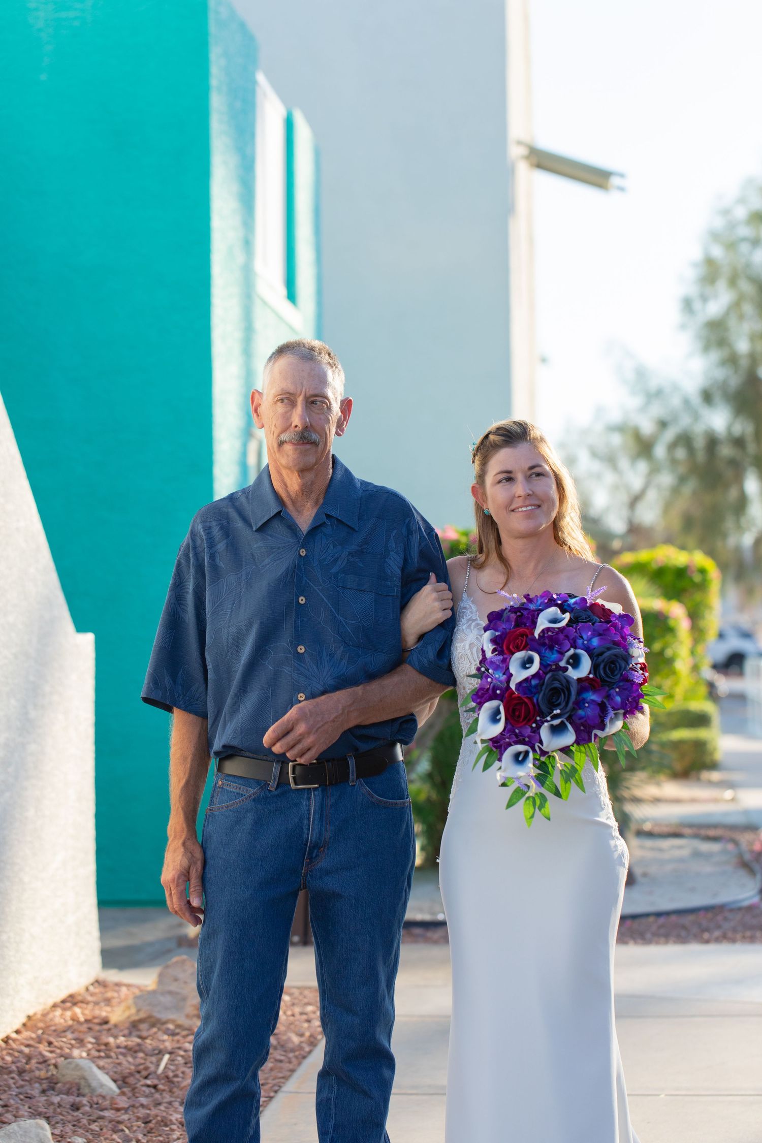 Father and daughter poses with vibrant purple bouquet outside turquoise wall at the nautical resort lake havasu before walking down aisle