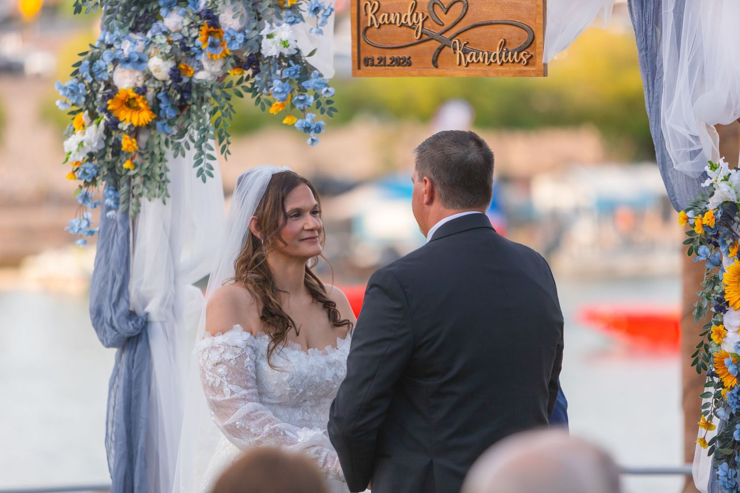 Bride and groom exchange vows at an outdoor waterfront wedding ceremony decorated with blue and yellow floral arrangements at Shugrues