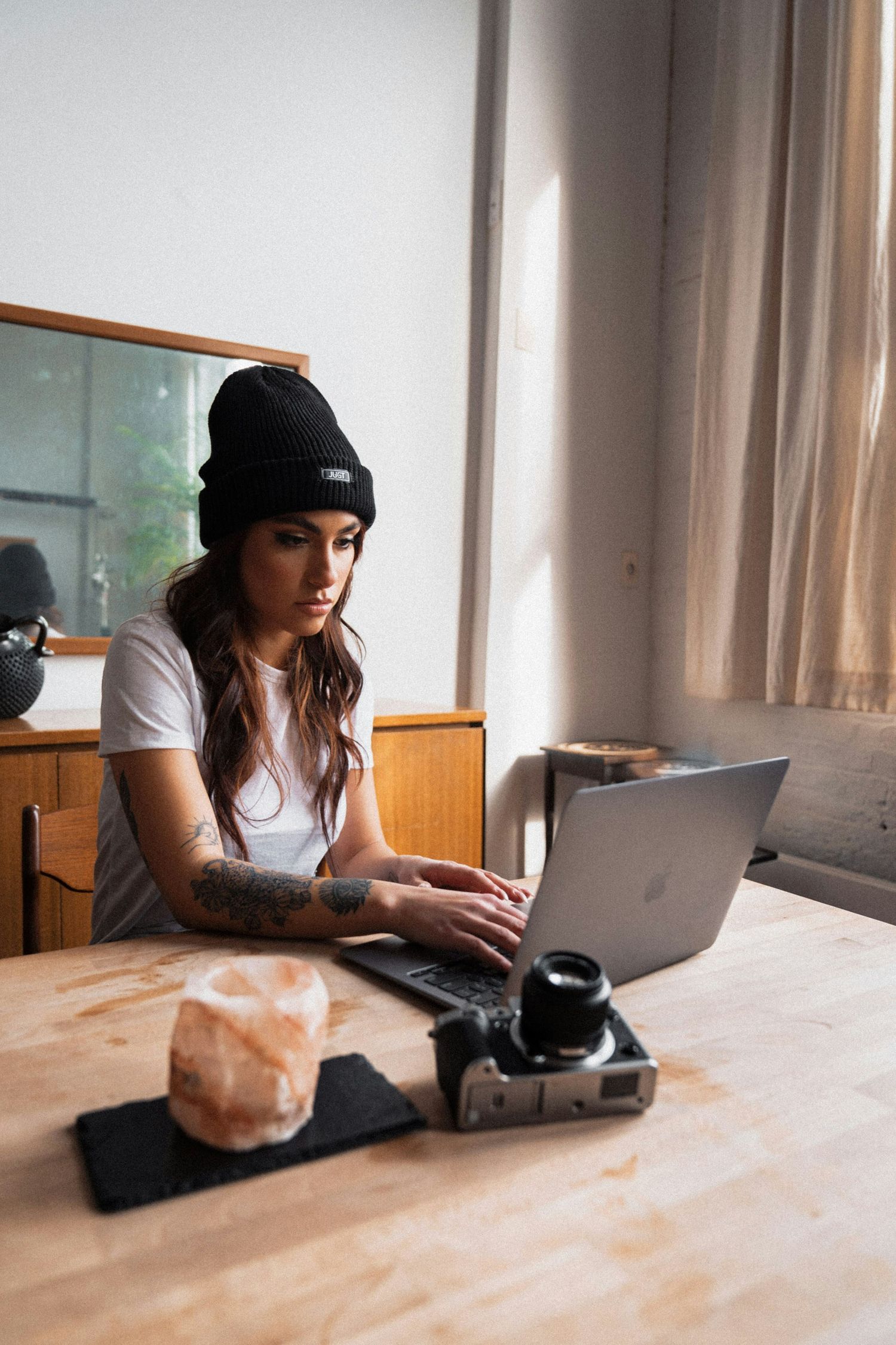 Creative workspace setup with laptop, camera and refreshments on wooden table.