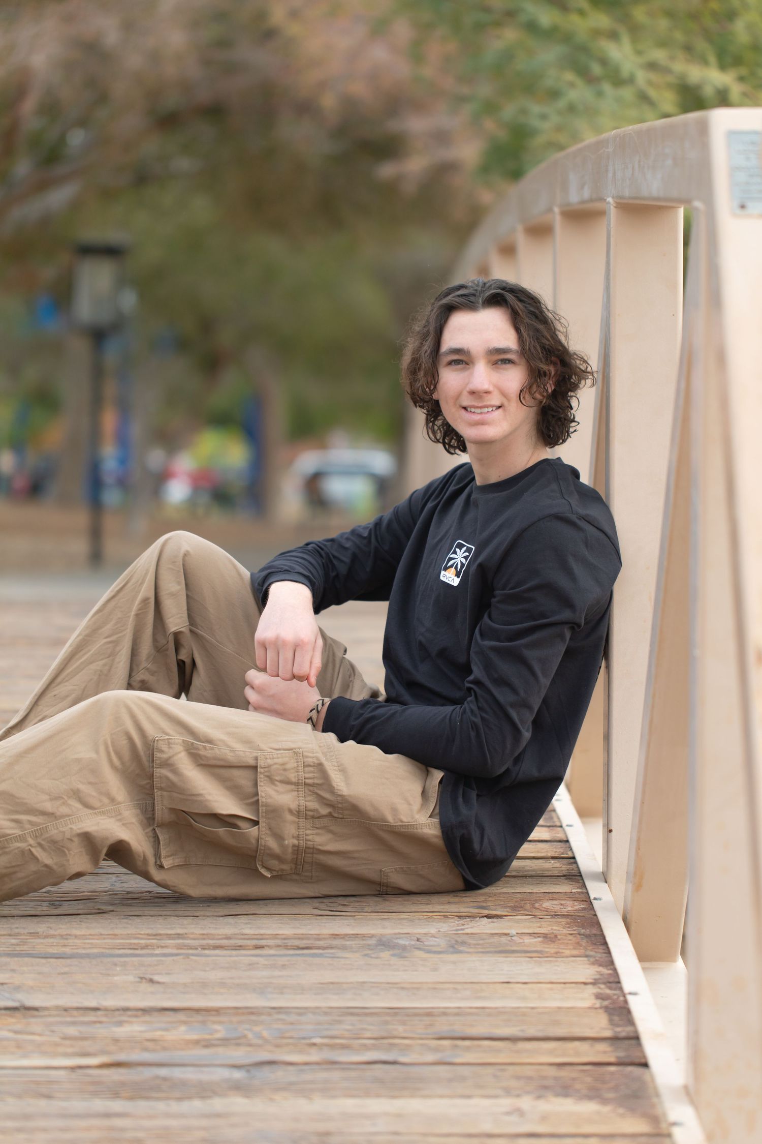 Young person in black hoodie relaxing on wooden bridge railing at rotary park in lake havasu in casual outdoor setting.