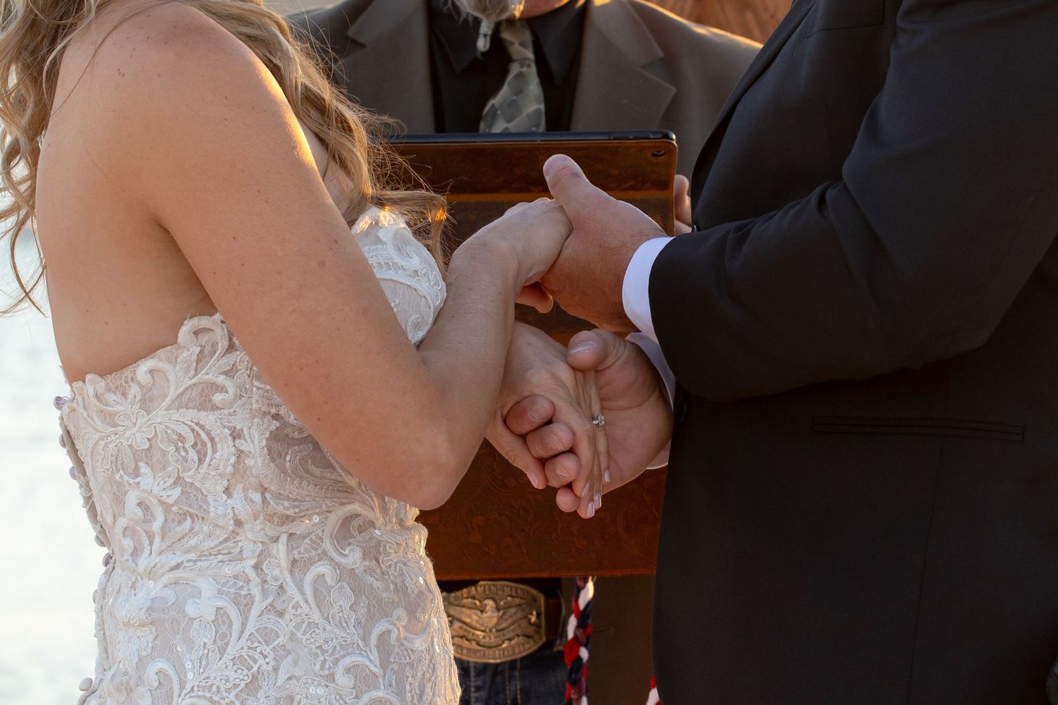 Close-up of couple holding hands during ceremony, lace dress and formal attire at Lake Havasu wedding.