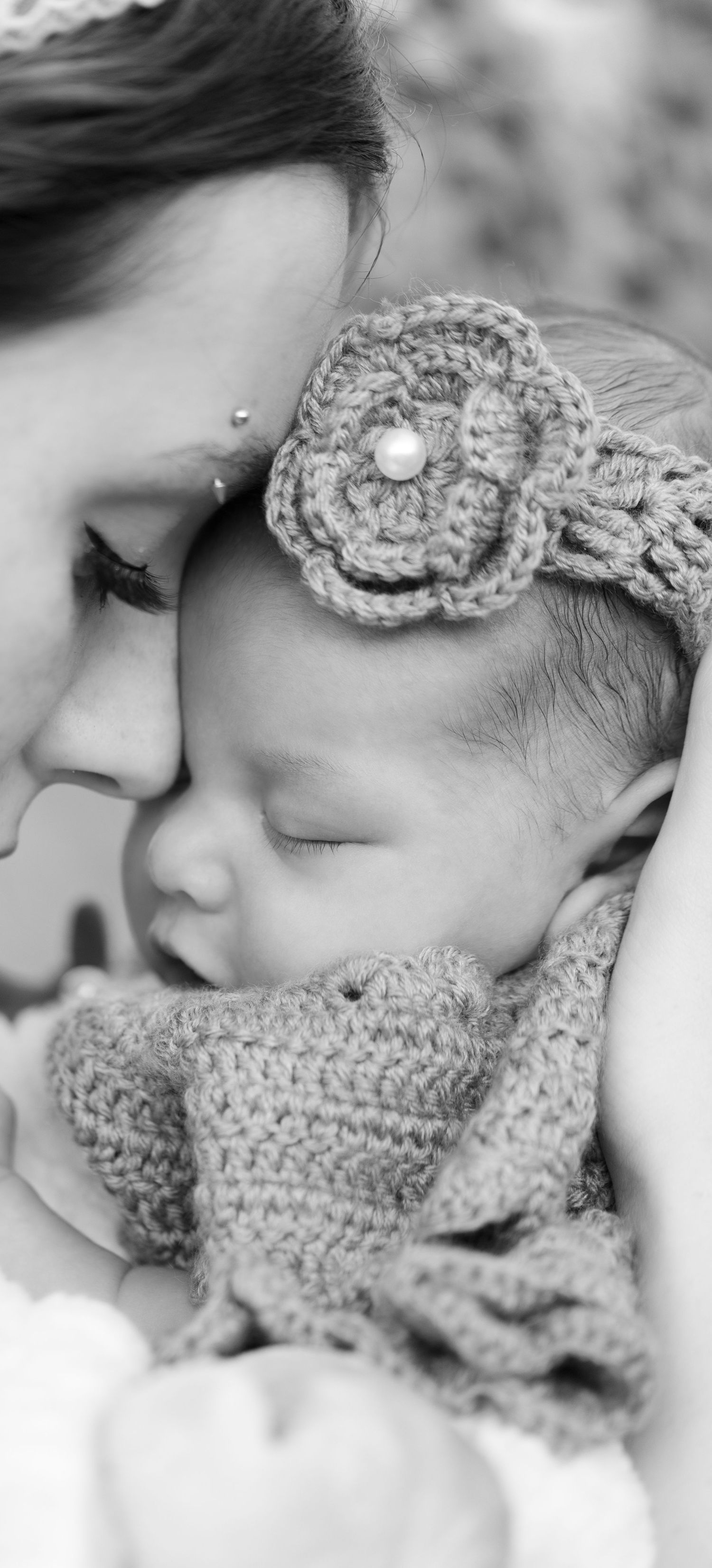 Black and white photo of a mother tenderly holding her sleeping newborn baby wearing a crochet flower headband.