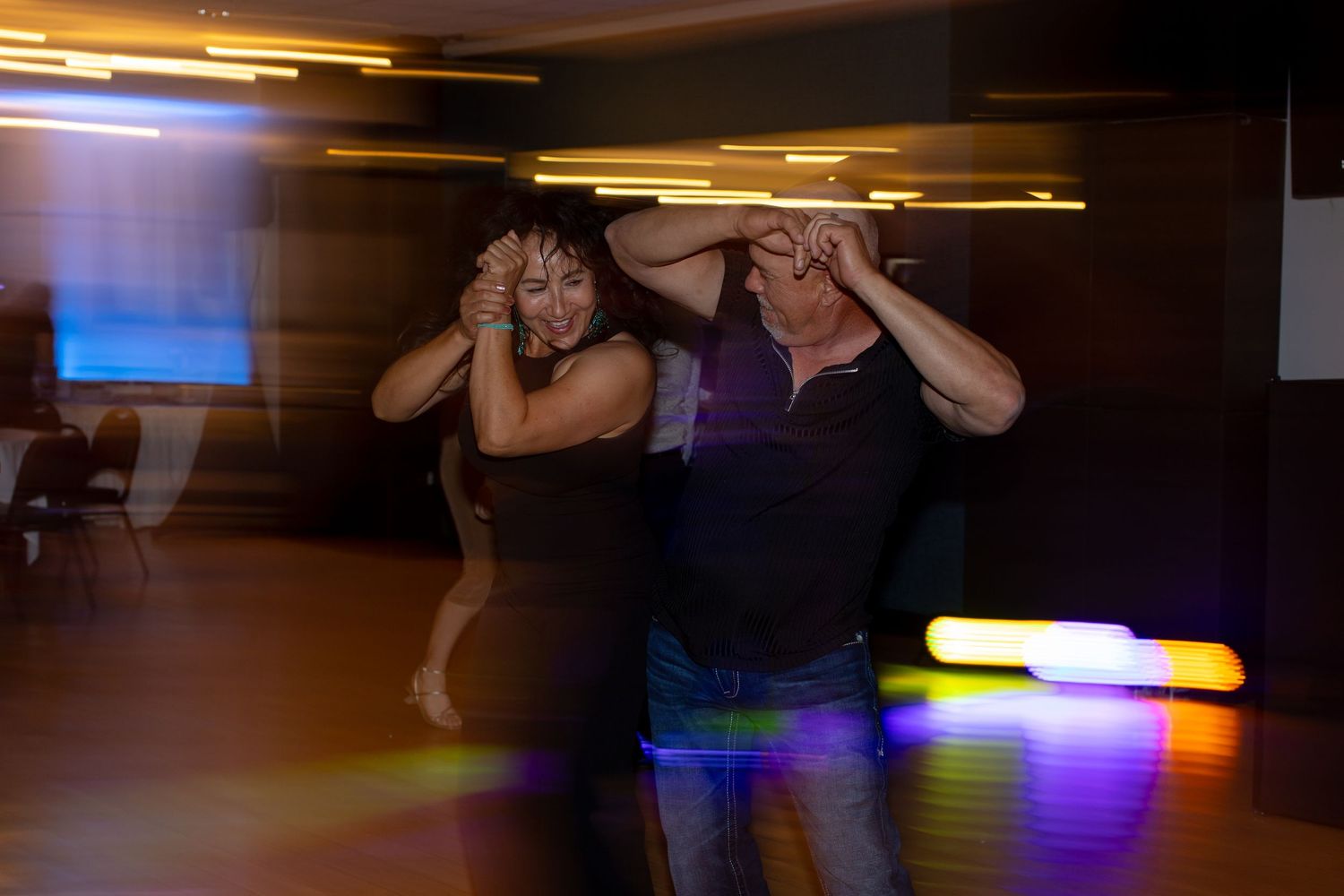 Two people dancing energetically together in a dimly lit dance hall with colorful lights in the background at Shugrues in Lake Havasu City