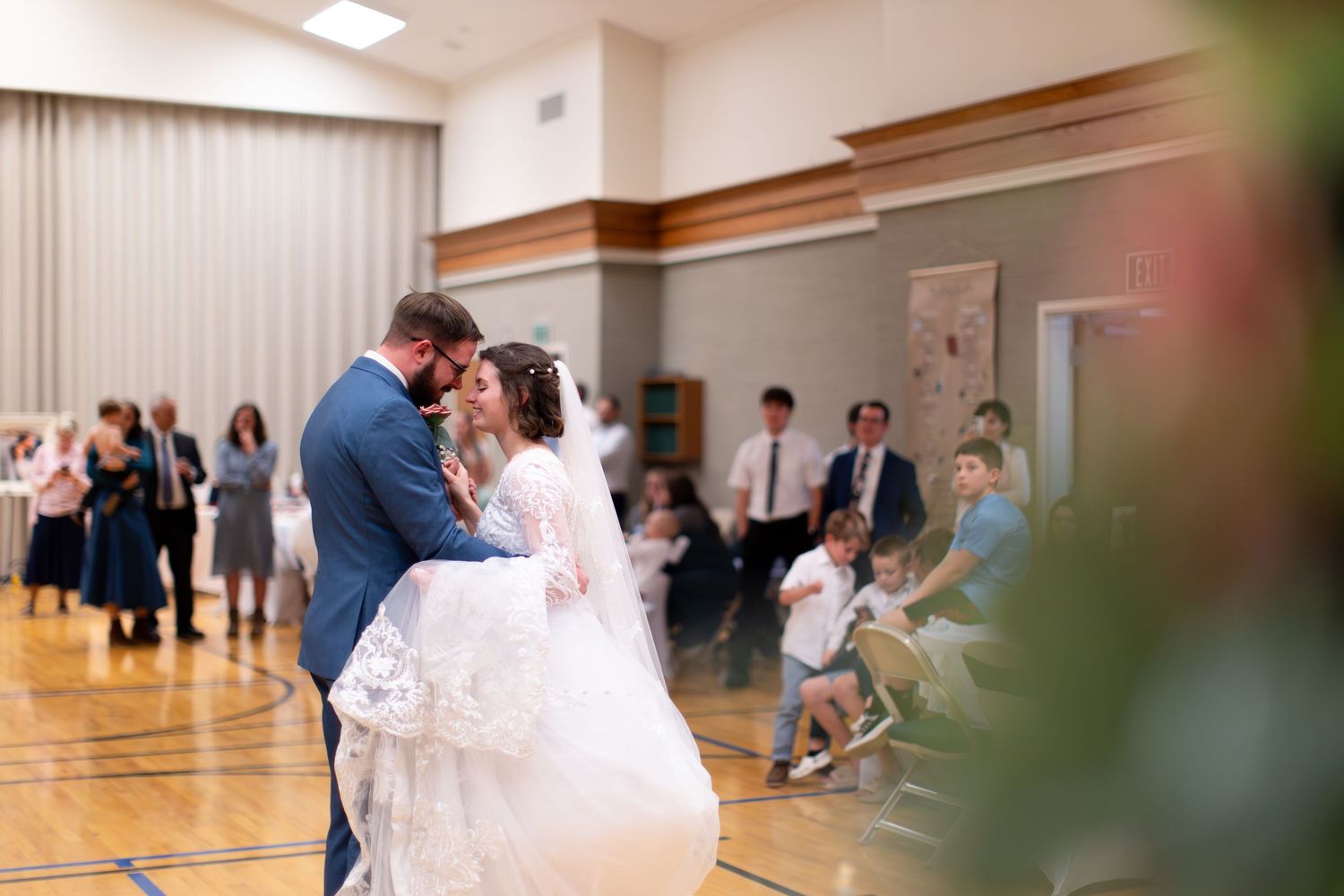 Wedding celebration in a bright indoor gymnasium with guests watching from the sides.