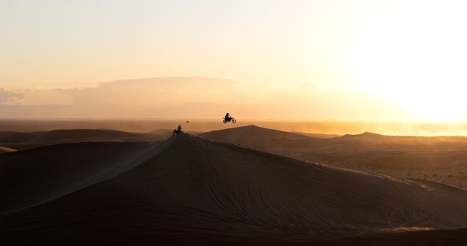 Silhouette of dirtbiker jumping off glamis desert Imperial sand dunes against a golden sunset sky creating dramatic shadows.