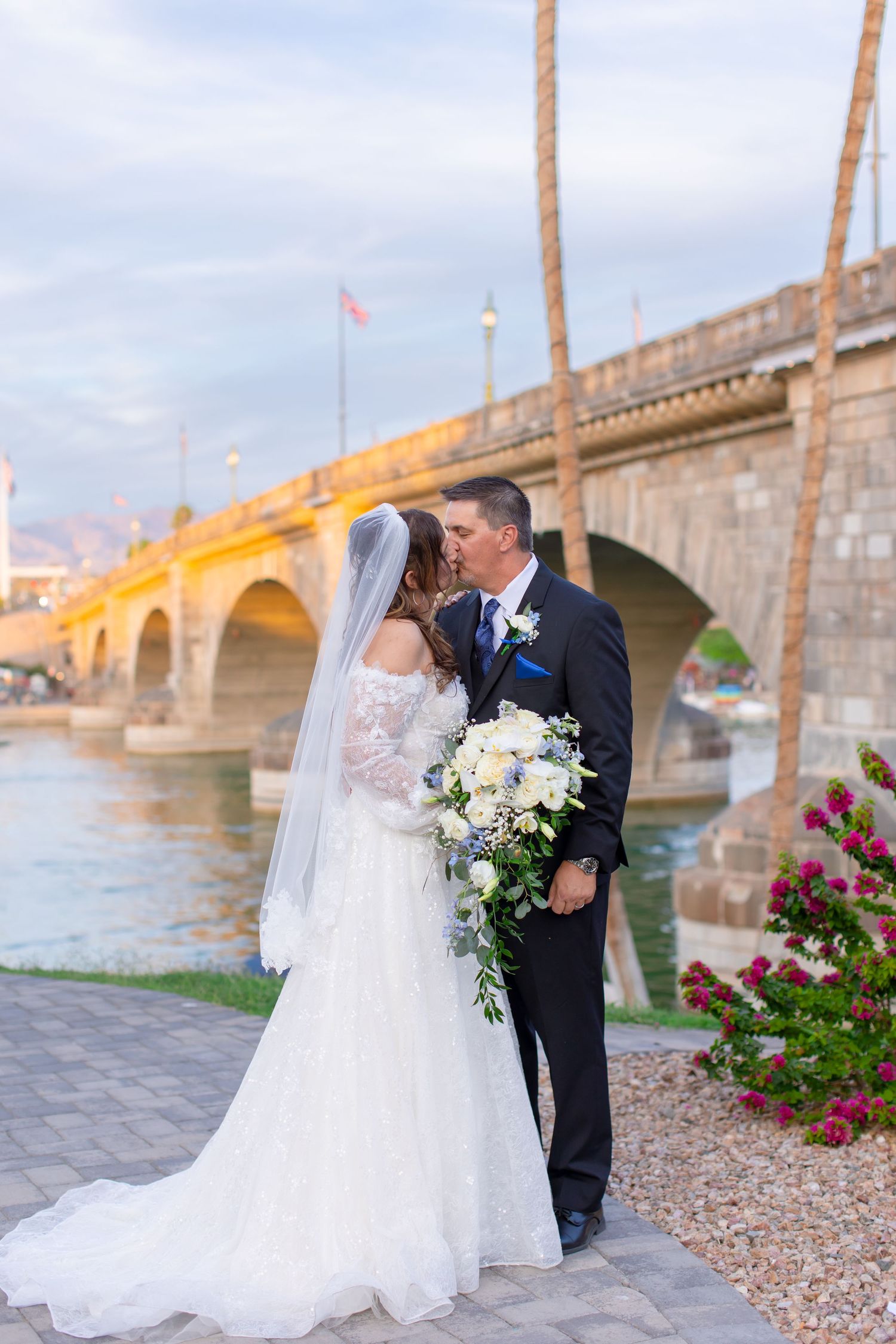 Bride and groom kissing by London Bridge in Lake Havasu City, AZ at sunset in elegant wedding attire.