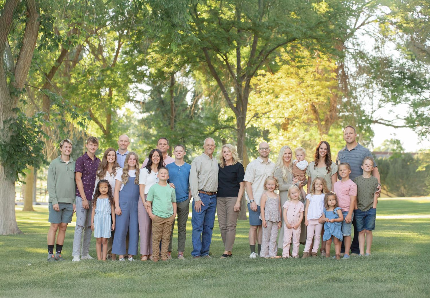 Large extended family group photo taken outdoors under trees during golden hour.