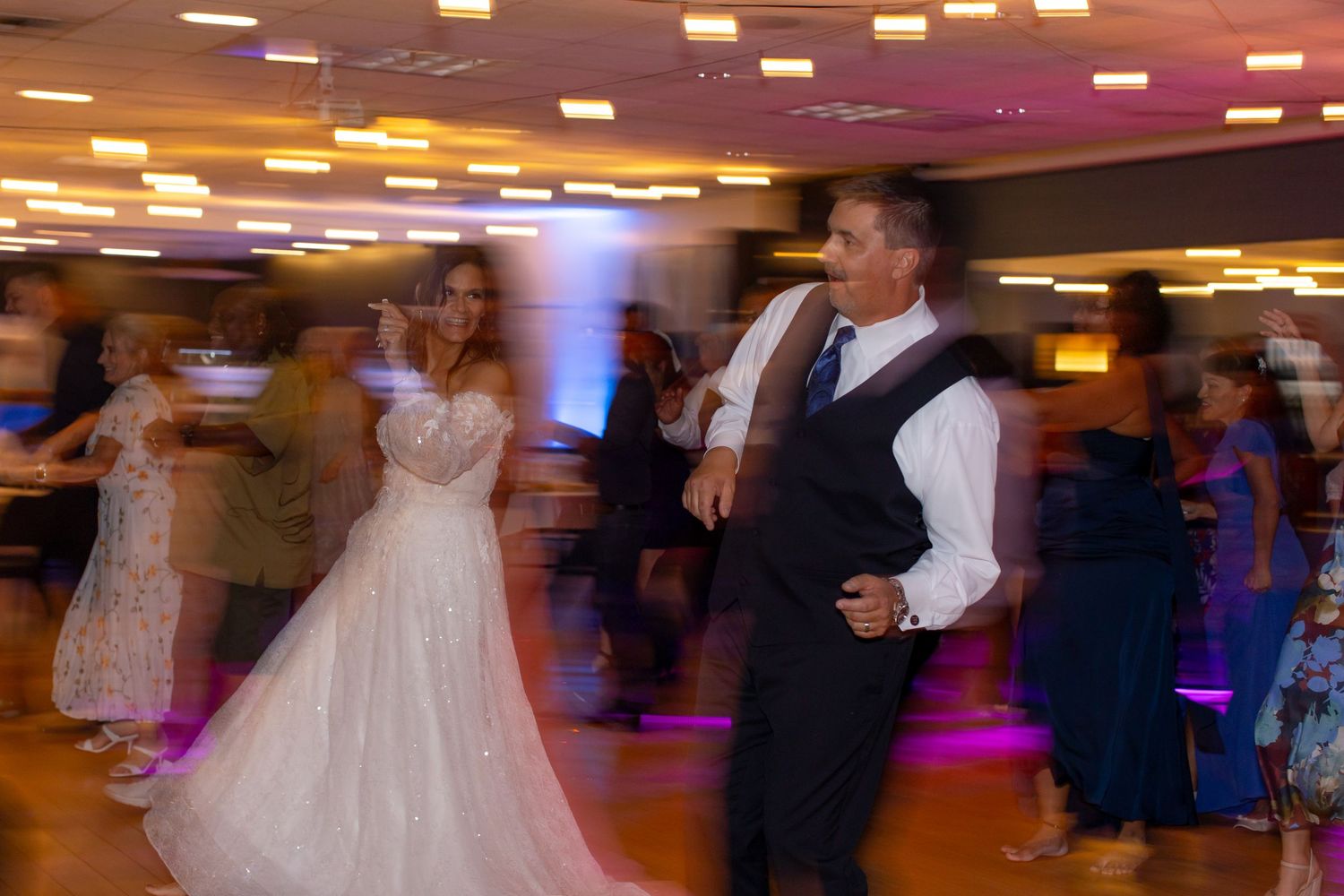 Bride in white gown dances joyfully with groom in vest at lively wedding reception dance floor at Shugrues in Lake Havasu