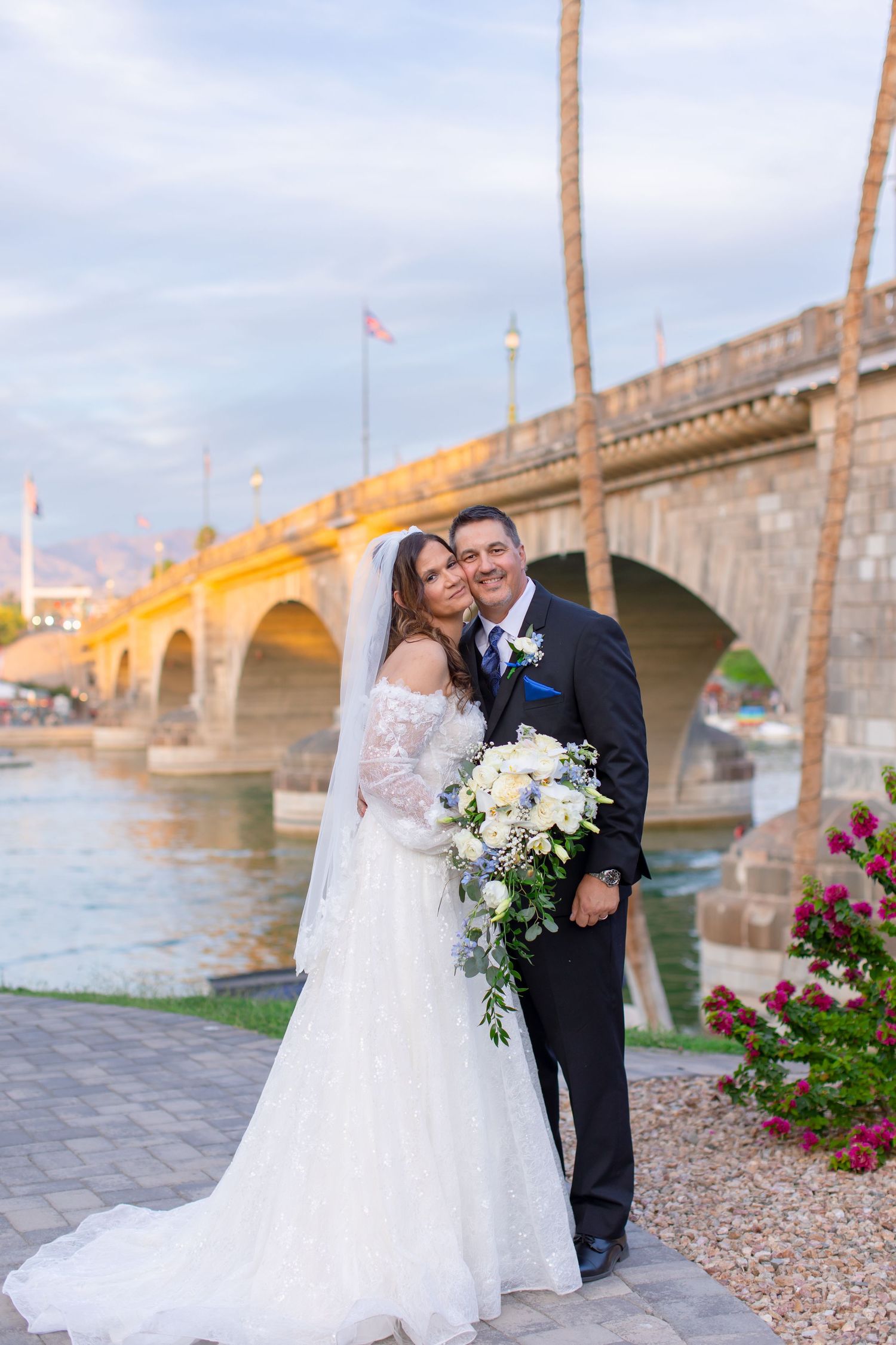 Bride and groom pose by London Bridge in Lake Havasu City, AZ, bride holding white floral bouquet at sunset at Shugrues