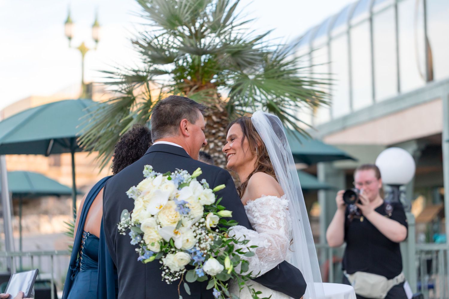 Bride and groom share a romantic moment at outdoor wedding ceremony, bride holding white and blue bouquet at Shugrues in Lake Havasu City
