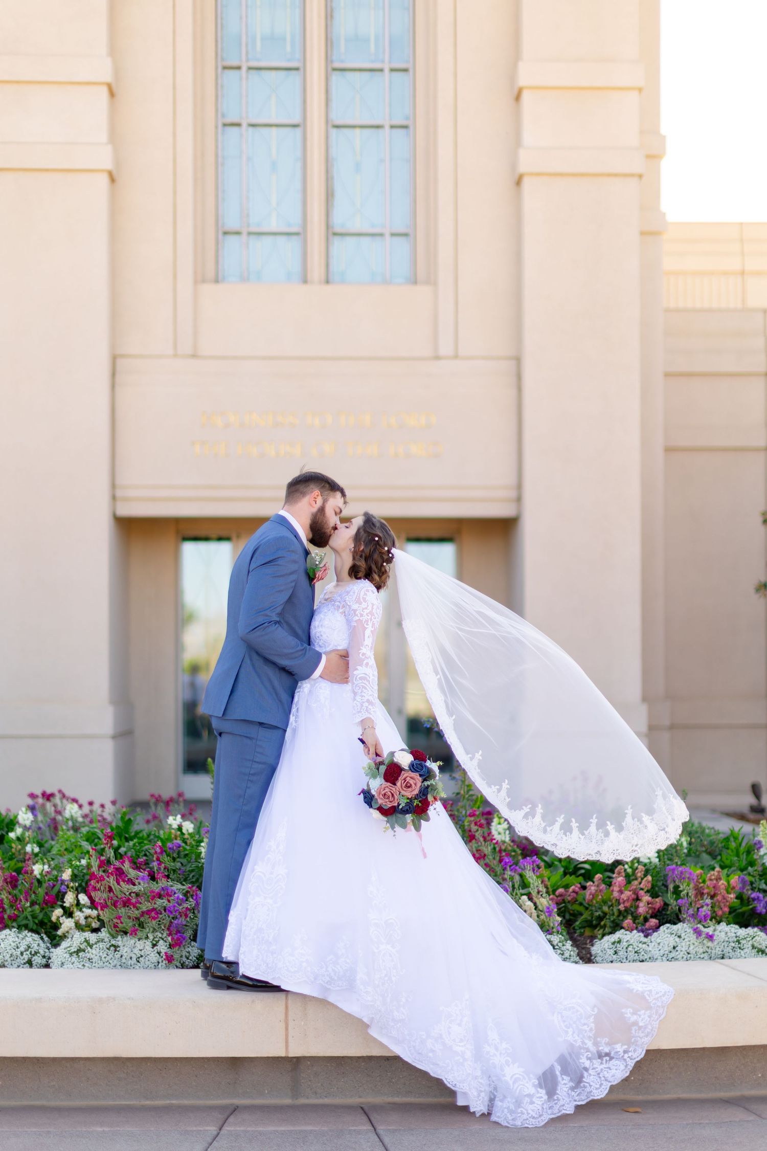 Bride and groom kissing in front of Gila Valley LDS temple with veil blowing in the wind behind them.