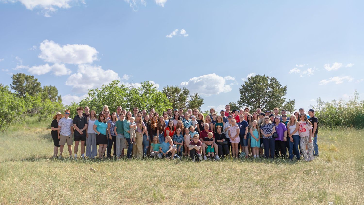A panoramic view of people gathered on a grassy hillside under blue skies with scattered clouds.