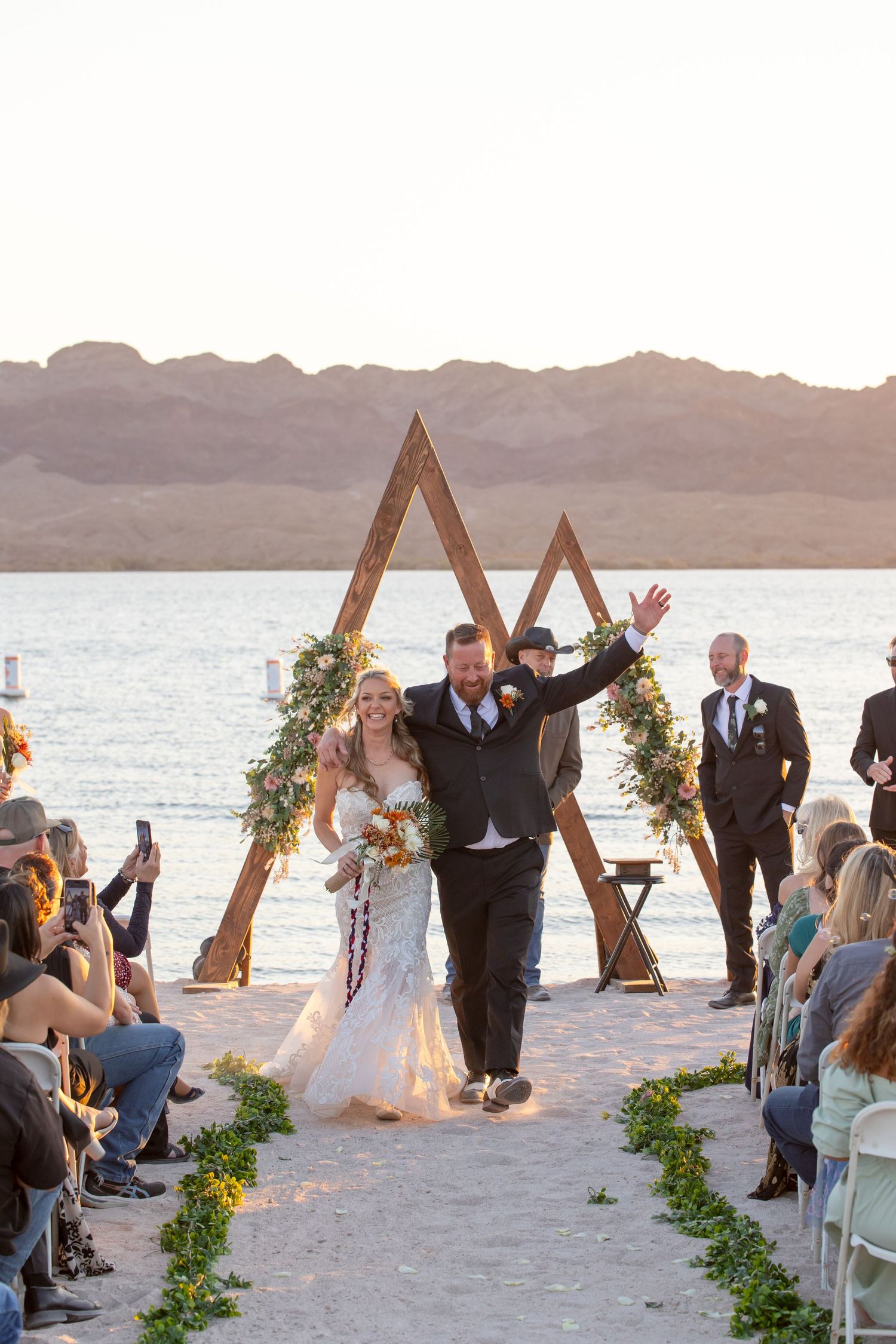 Outdoor beach wedding ceremony with wooden triangle arch decorated with greenery and flowers at the riviera marina lake havasu