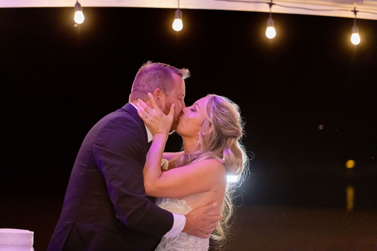 A romantic kiss between newlyweds under string lights during their evening wedding reception at the Riviera Marina in Lake Havasu City AZ.
