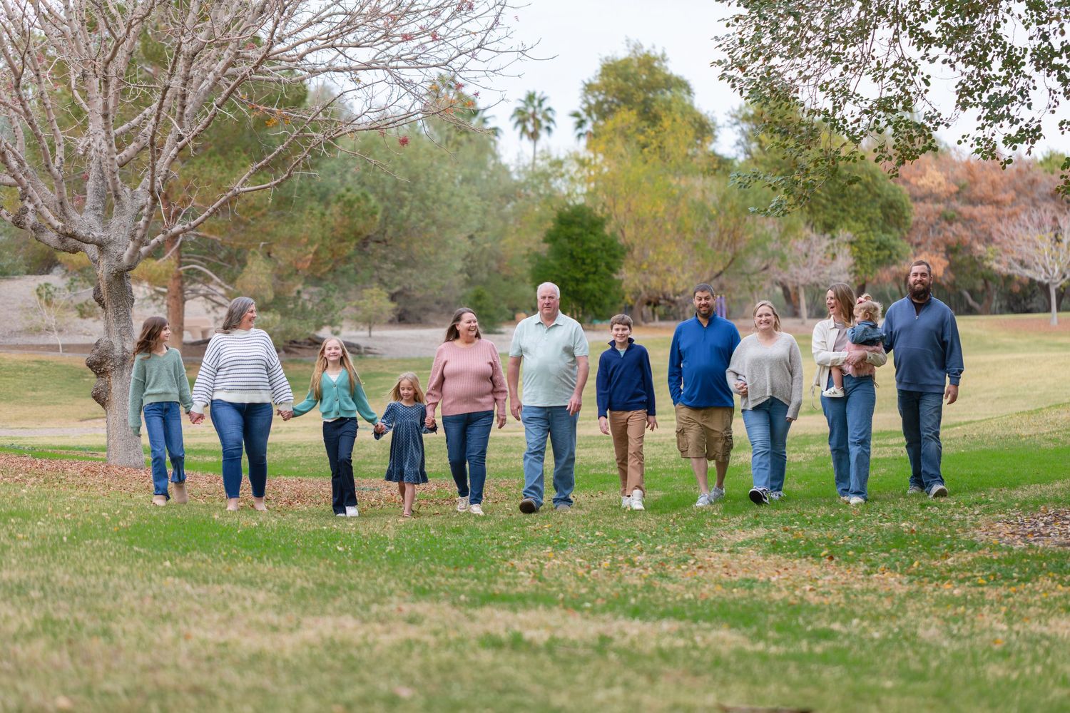 A group of people wearing blue jeans walk together in a line across a grassy field during autumn at Rotary Park Lake Havasu